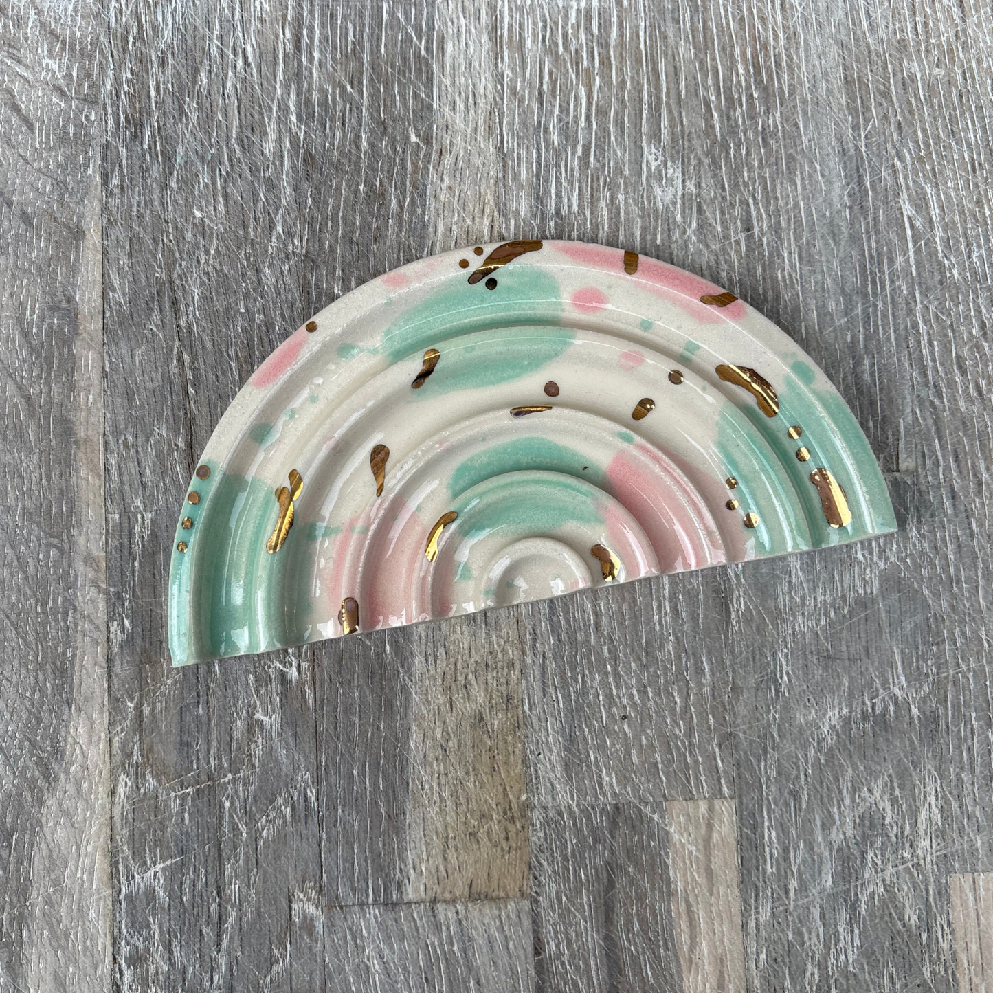 Decorative rainbow-shaped soap dishes with gold accents on a wooden surface