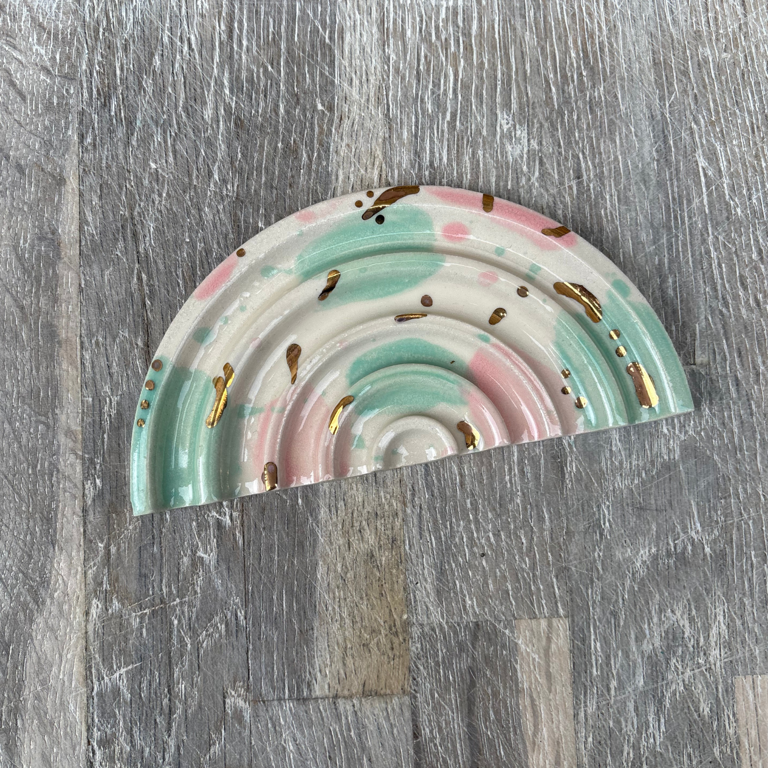 Decorative rainbow-shaped soap dishes with gold accents on a wooden surface