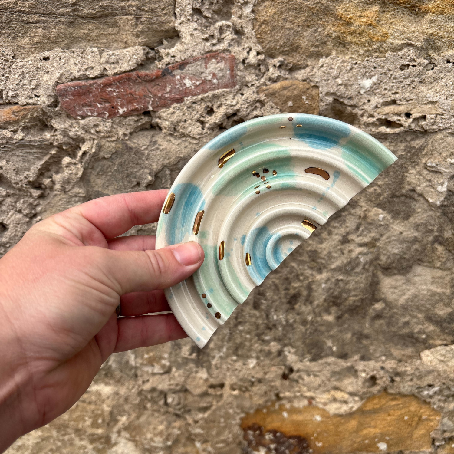 Hand holding a ceramic soap dishes with a wave design against a stone wall background
