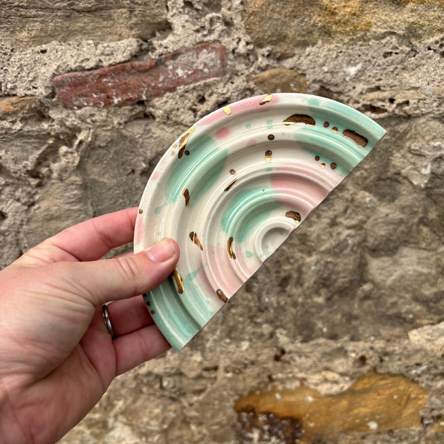 Hand holding a decorative ceramic soap dishes with a stone wall background