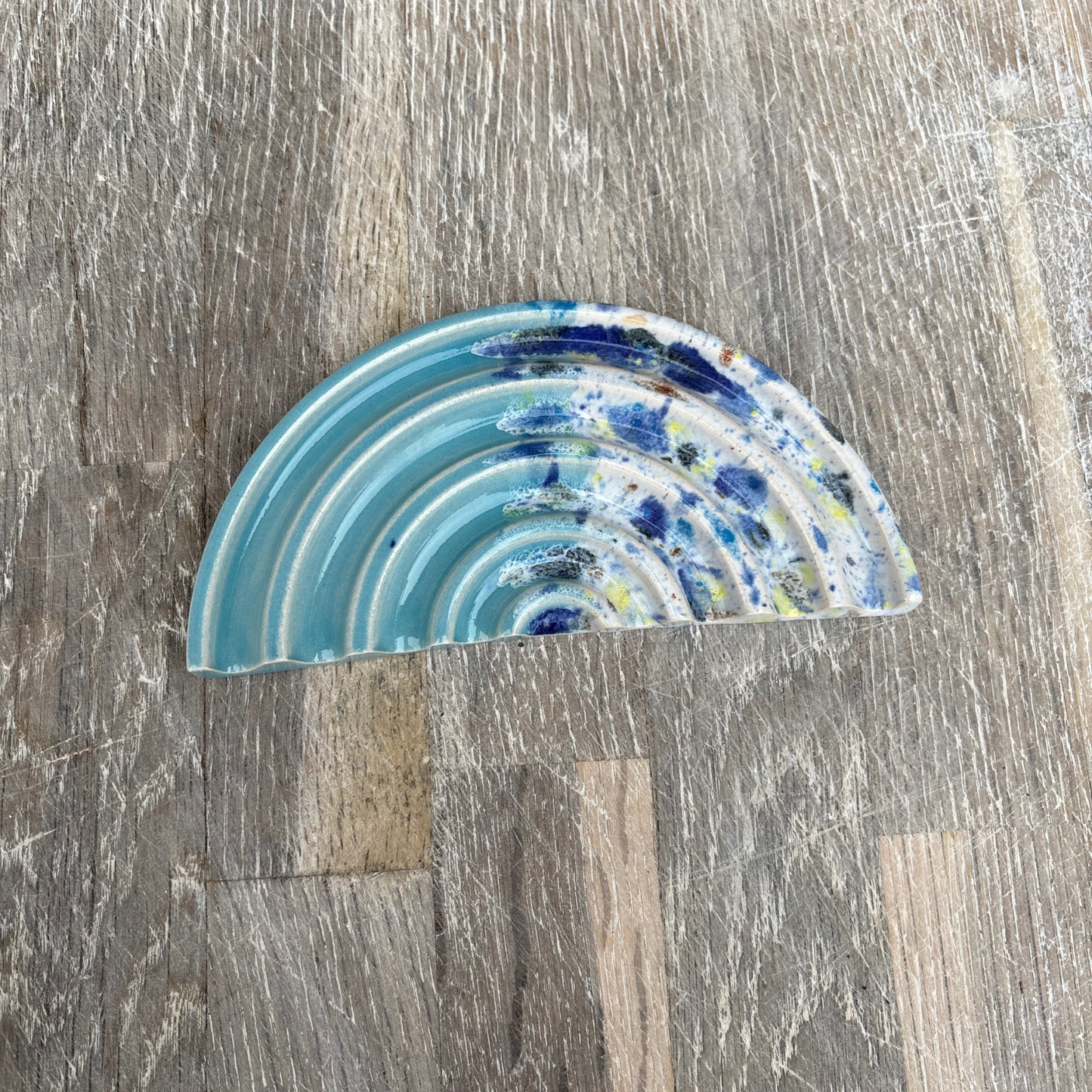 Semicircular ceramic soap dish with blue and white concentric pattern on a wooden surface