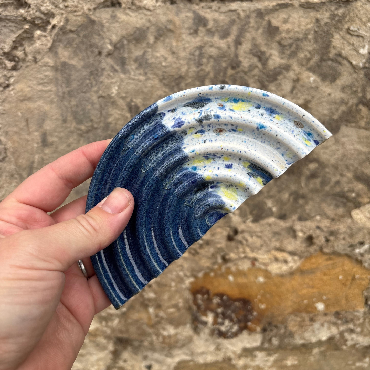 Hand holding a ceramic soap dish with blue and white swirl pattern against a stone background