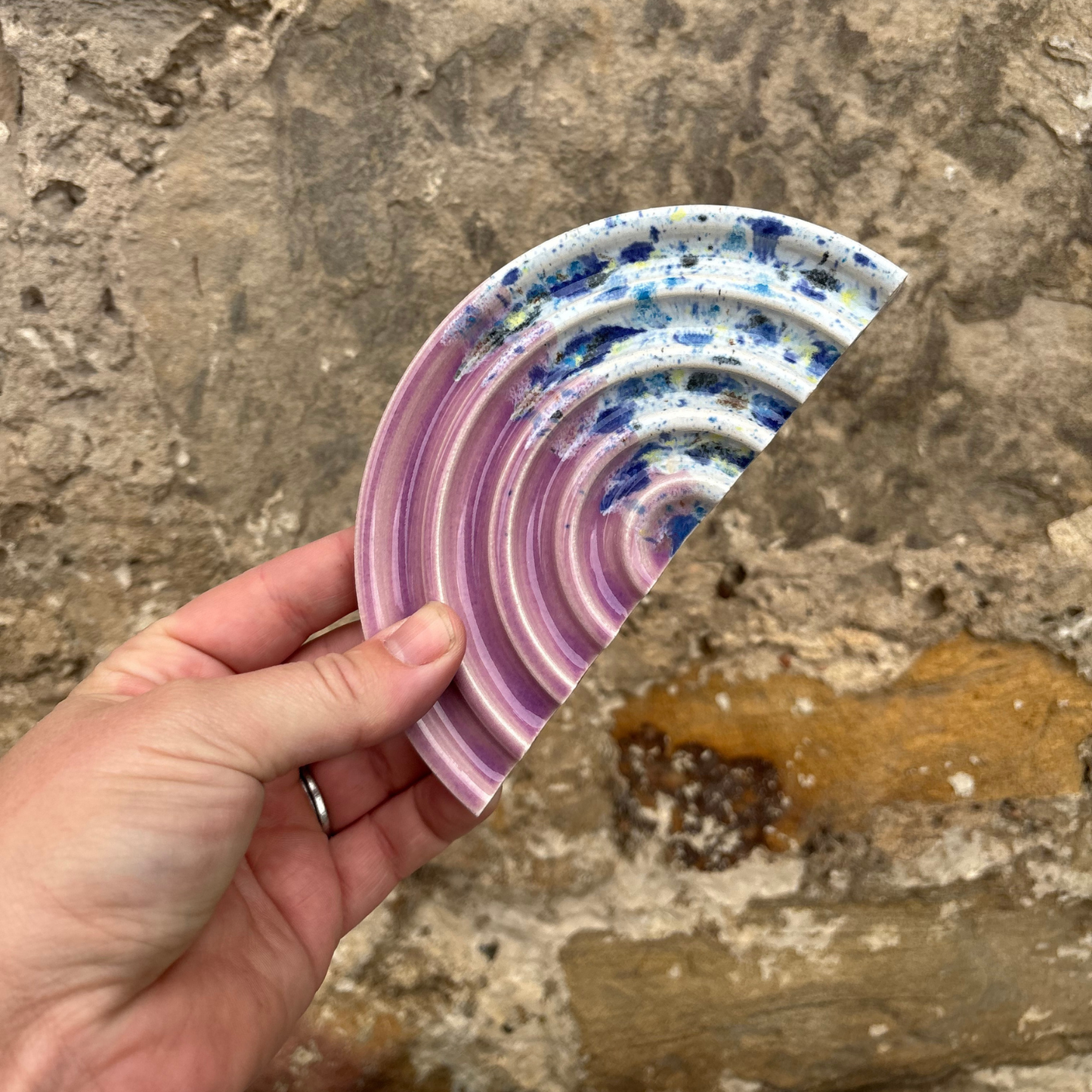 Hand holding a colourful, textured circular soap dish against a stone background
