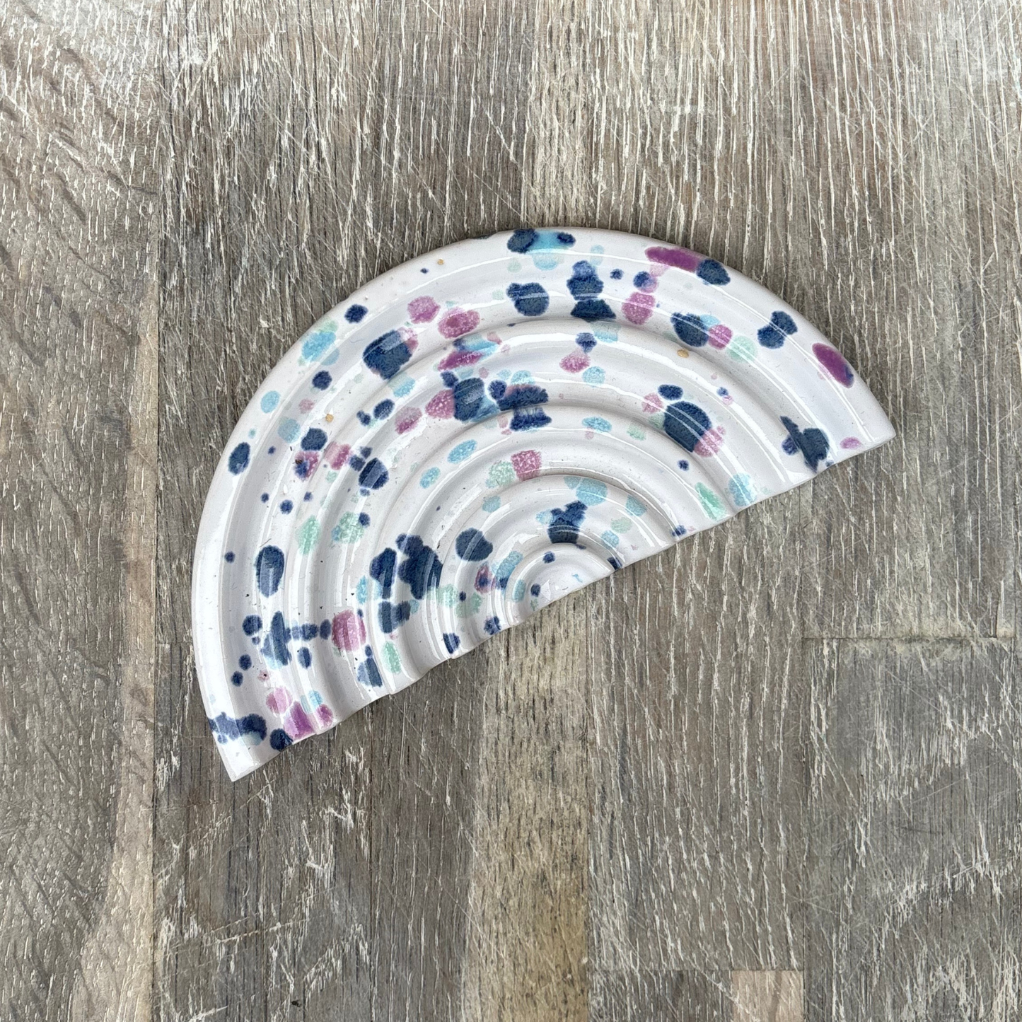 Half-circle ceramic soap dish with colorful dot pattern on a wooden surface