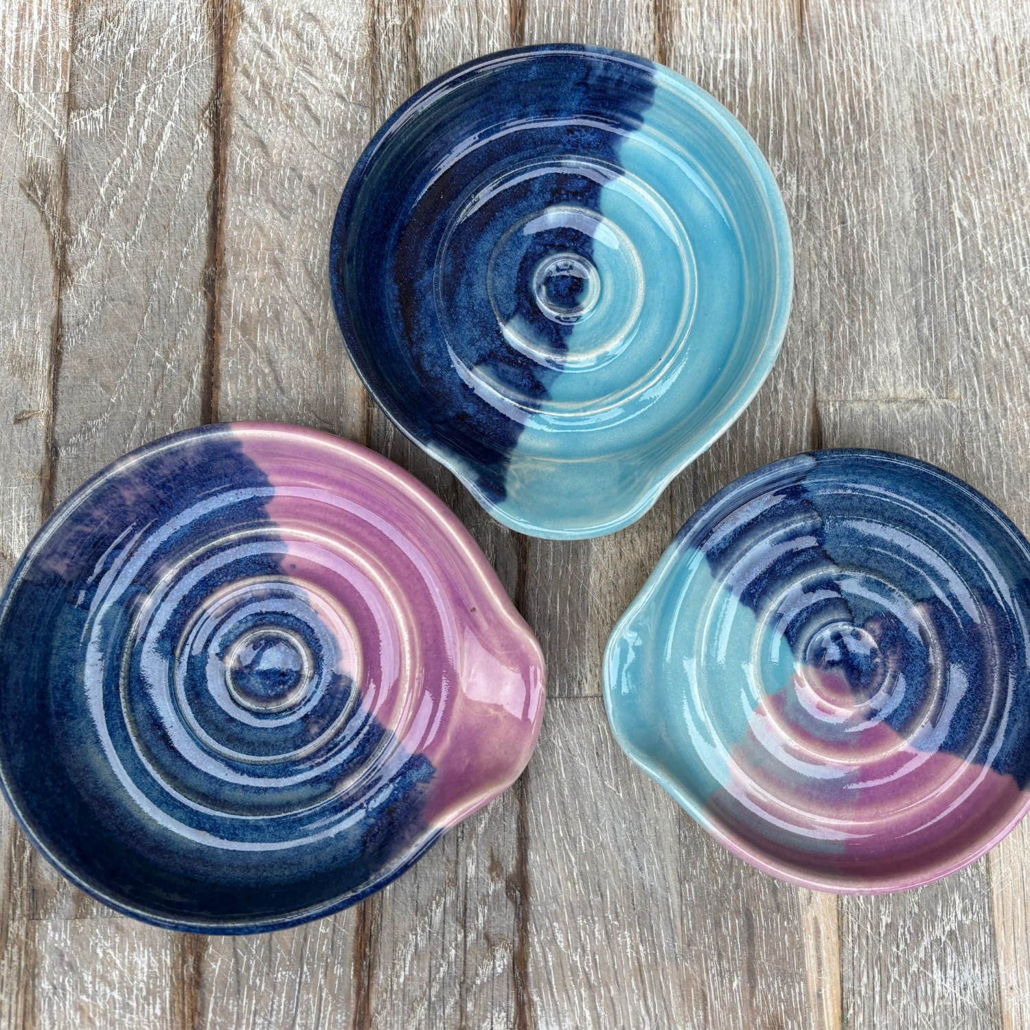 Three ceramic bowls with concentric circle patterns in blue, pink, and purple on a wooden surface.