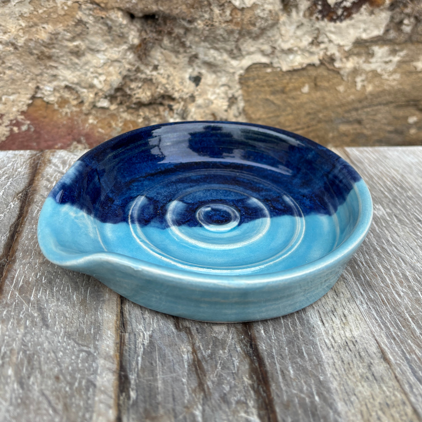 Blue ceramic dish on a wooden surface with a stone wall background