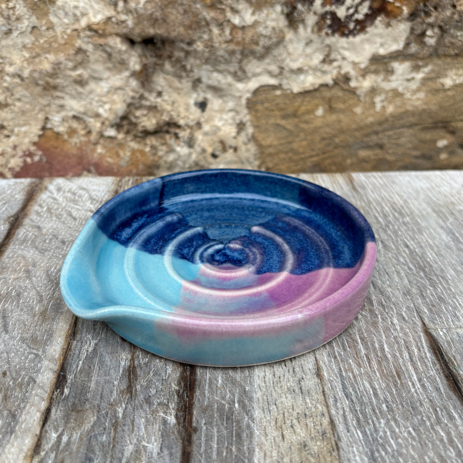 Ceramic spoon rest dish with blue and pink spiral design on a wooden surface