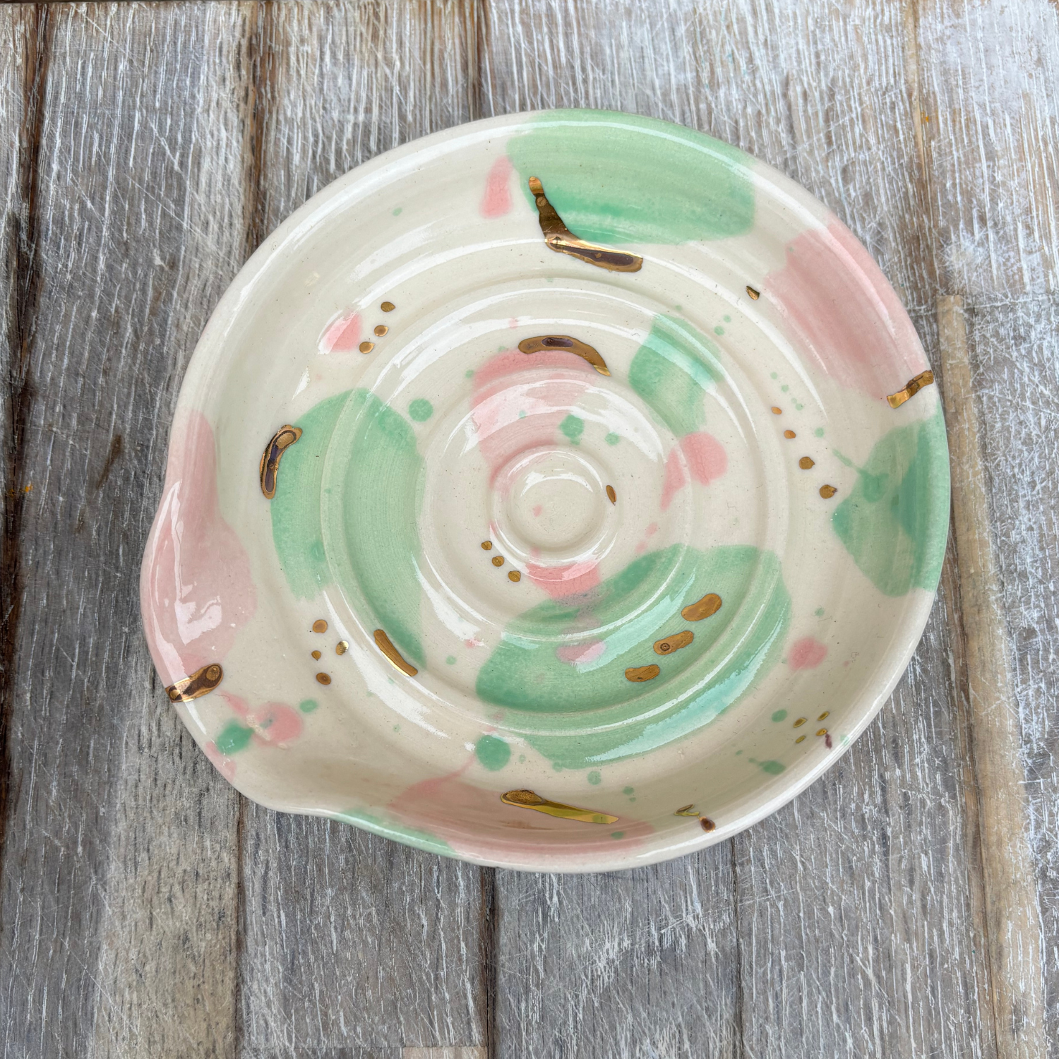 Decorative ceramic plate with pink and green design on a wooden surface