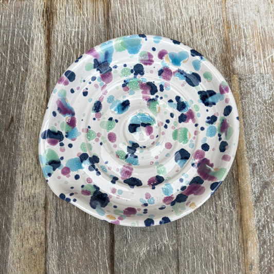 Decorative ceramic plate with multicolored dot pattern on a wooden surface