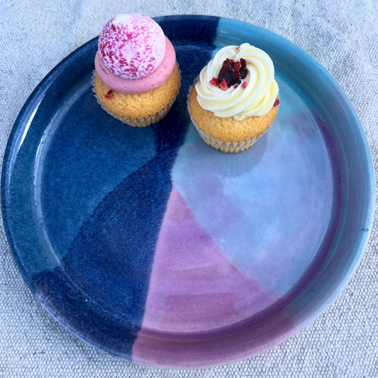 Two cupcakes with pink and white frosting on a blue and purple plate.