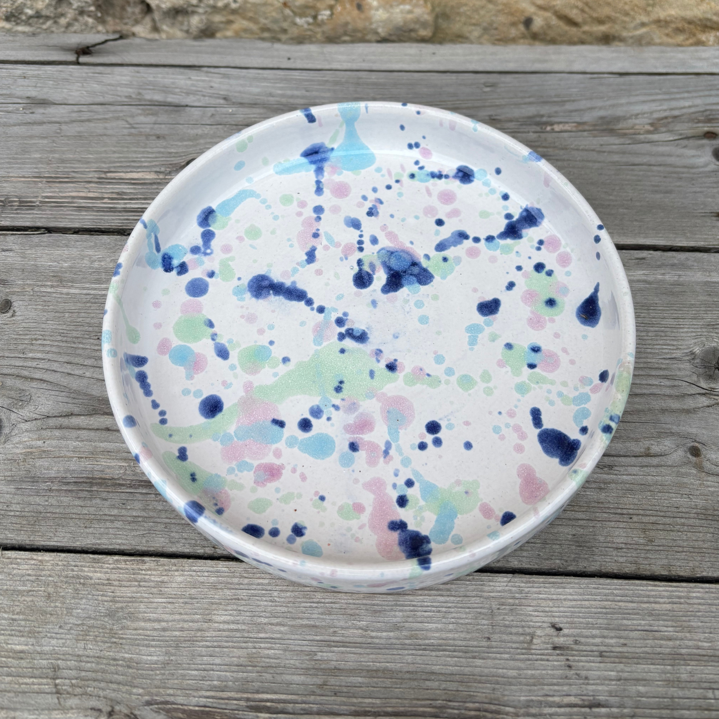 Round ceramic plate with colorful splatter design on a wooden surface