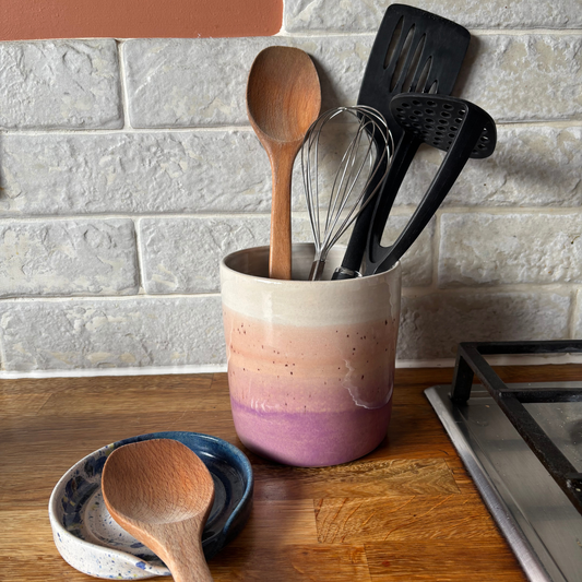Colorful ceramic utensil holder with kitchen utensils on a wooden countertop.