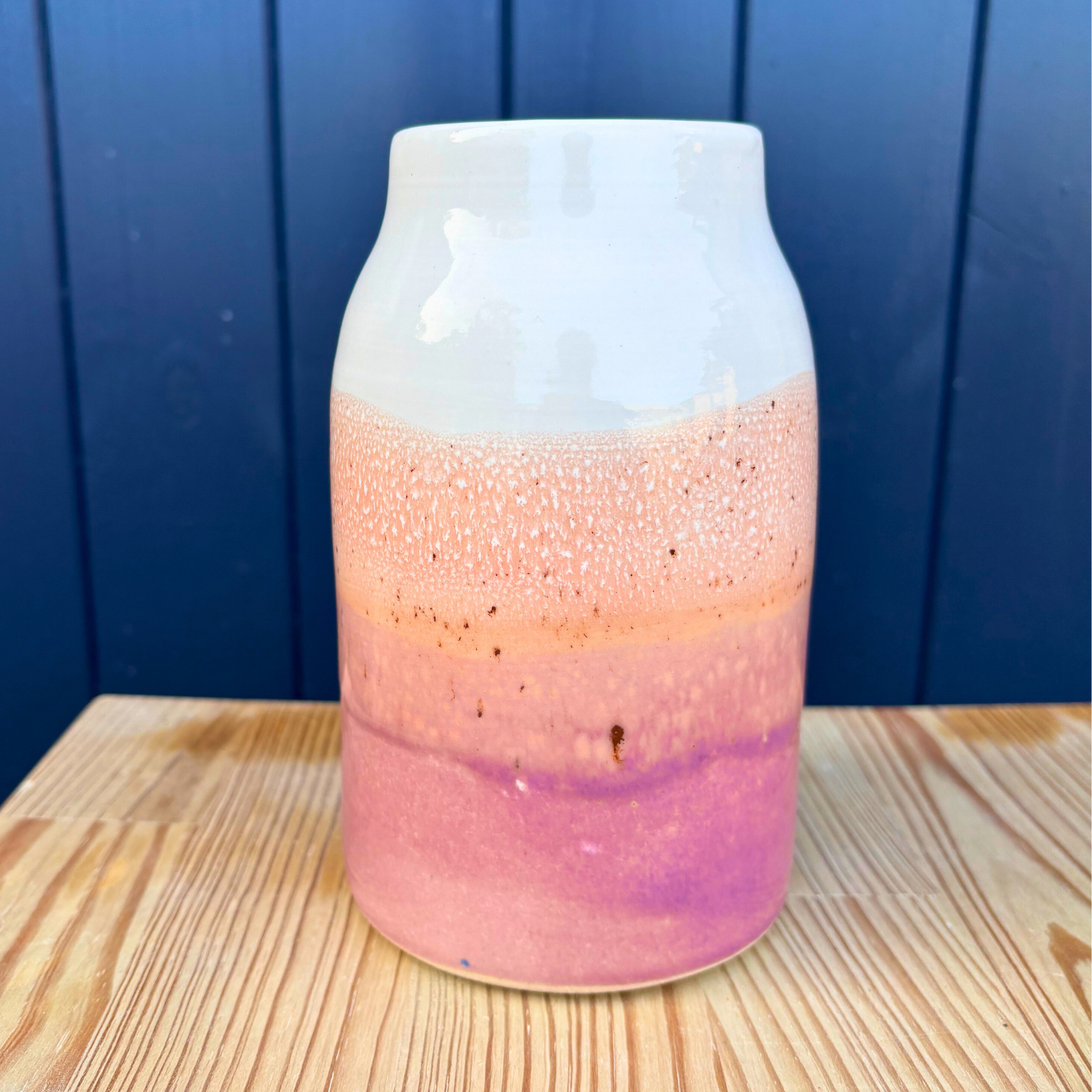 Vase with gradient color from white to pink on a wooden surface with blue background
