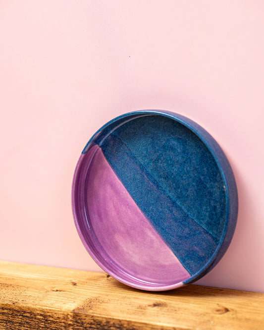 Two-toned purple and blue ceramic plate on a wooden surface with a pink background