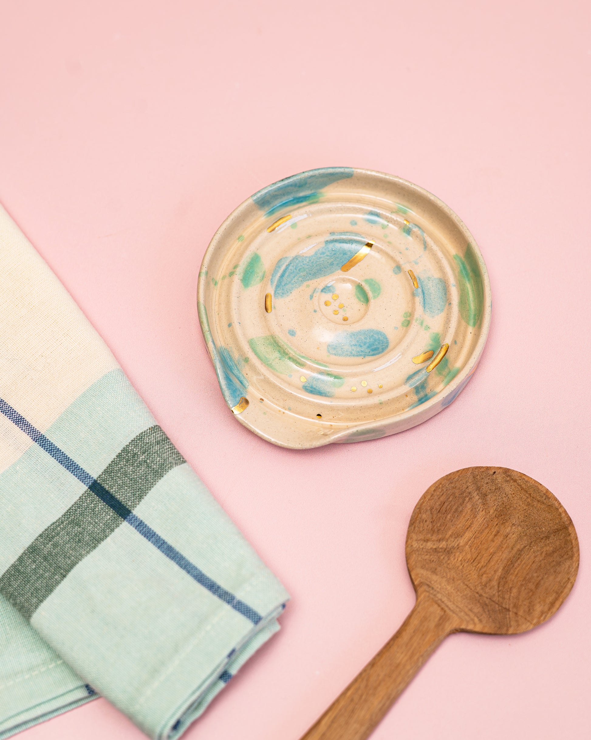 Ceramic dish, wooden spoon, and checkered towel on a pink background