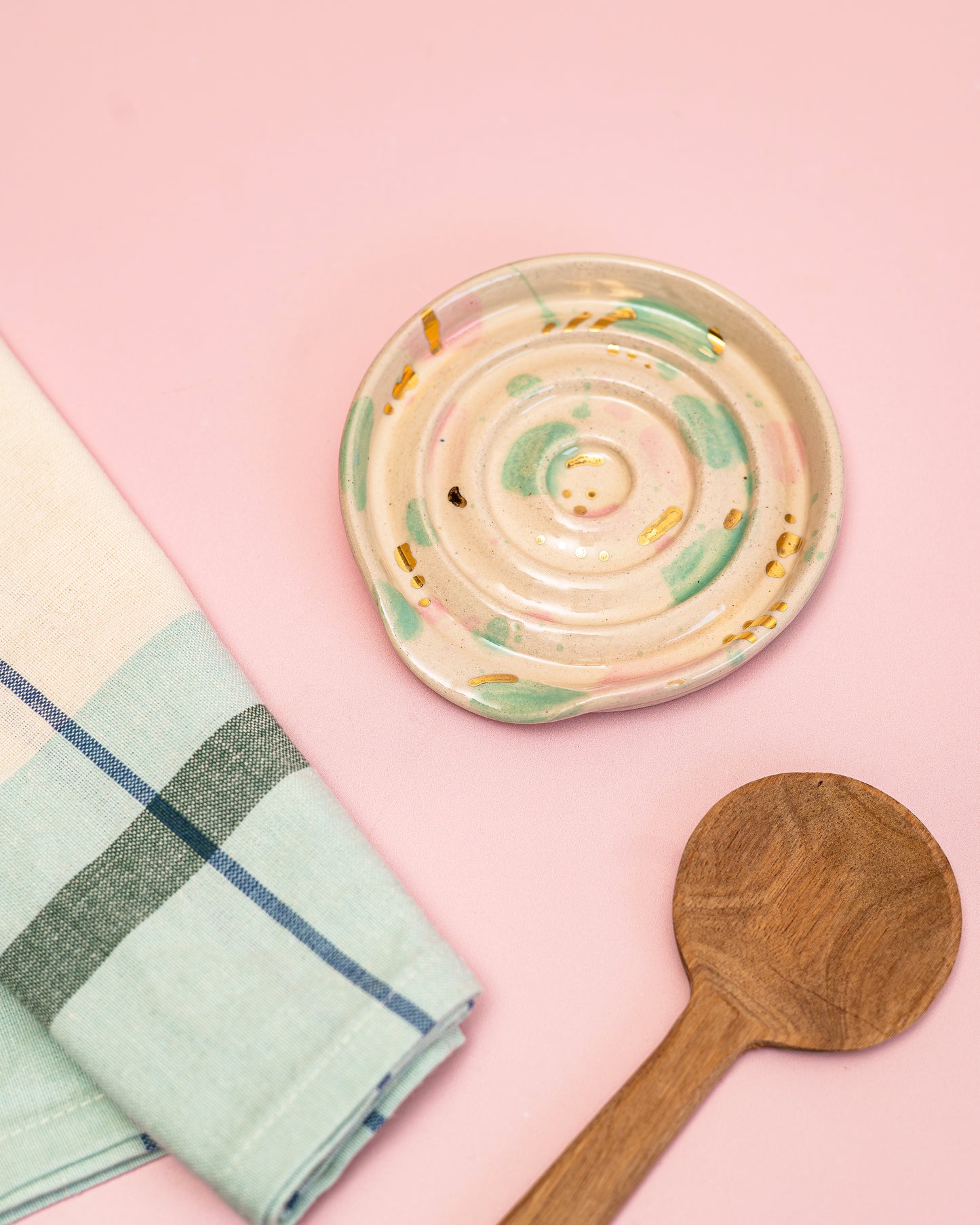 Ceramic dish, wooden spoon, and checkered towel on a pink background
