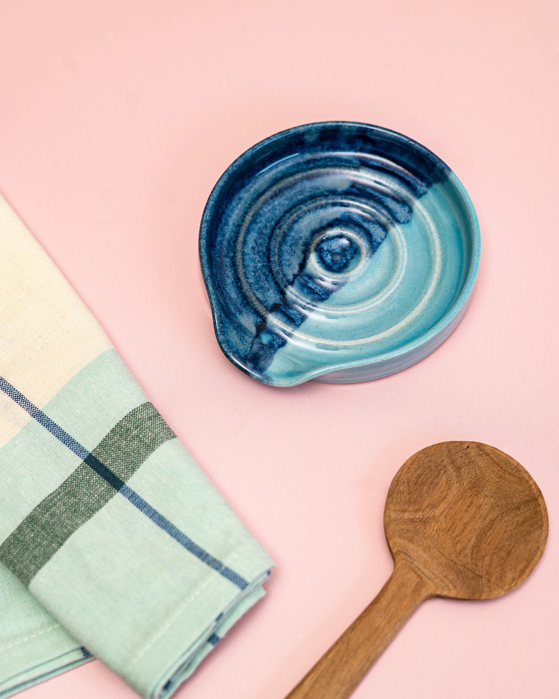 Blue ceramic dish, wooden spoon, and checkered towel on a pink background