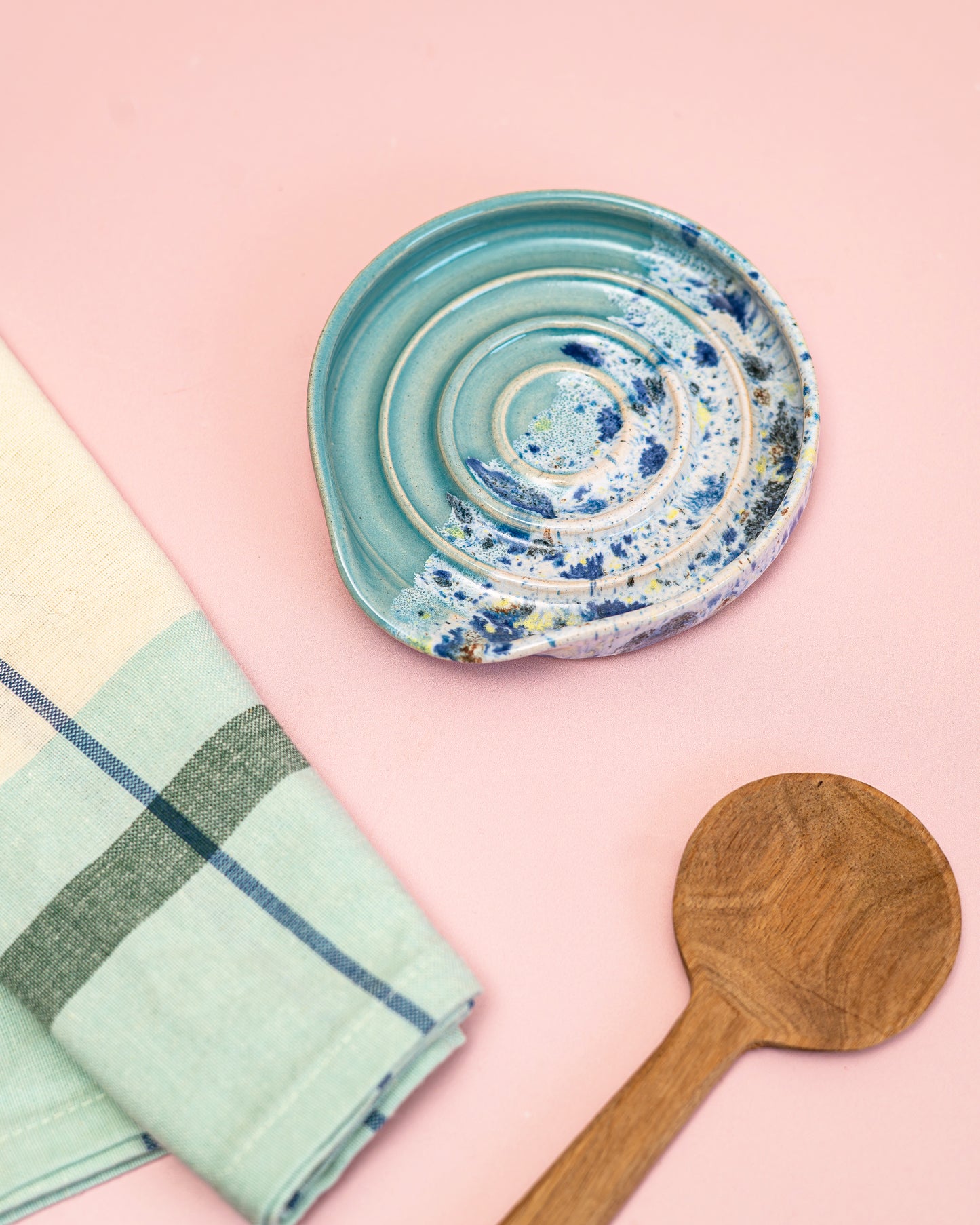 Decorative ceramic plate with a wooden spoon and checkered towel on a pink background