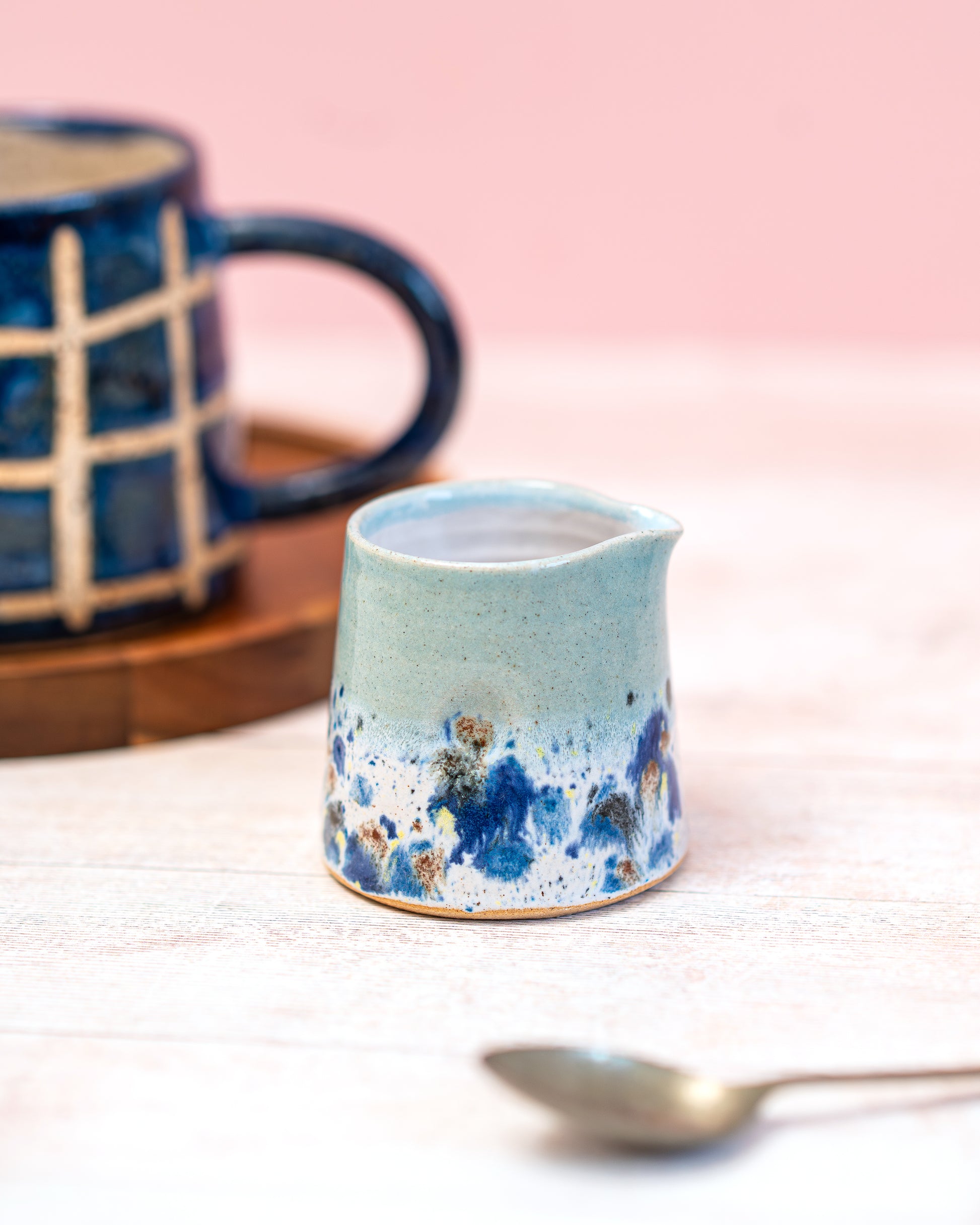 Ceramic creamer with blue speckled design on a light surface with a blurred background