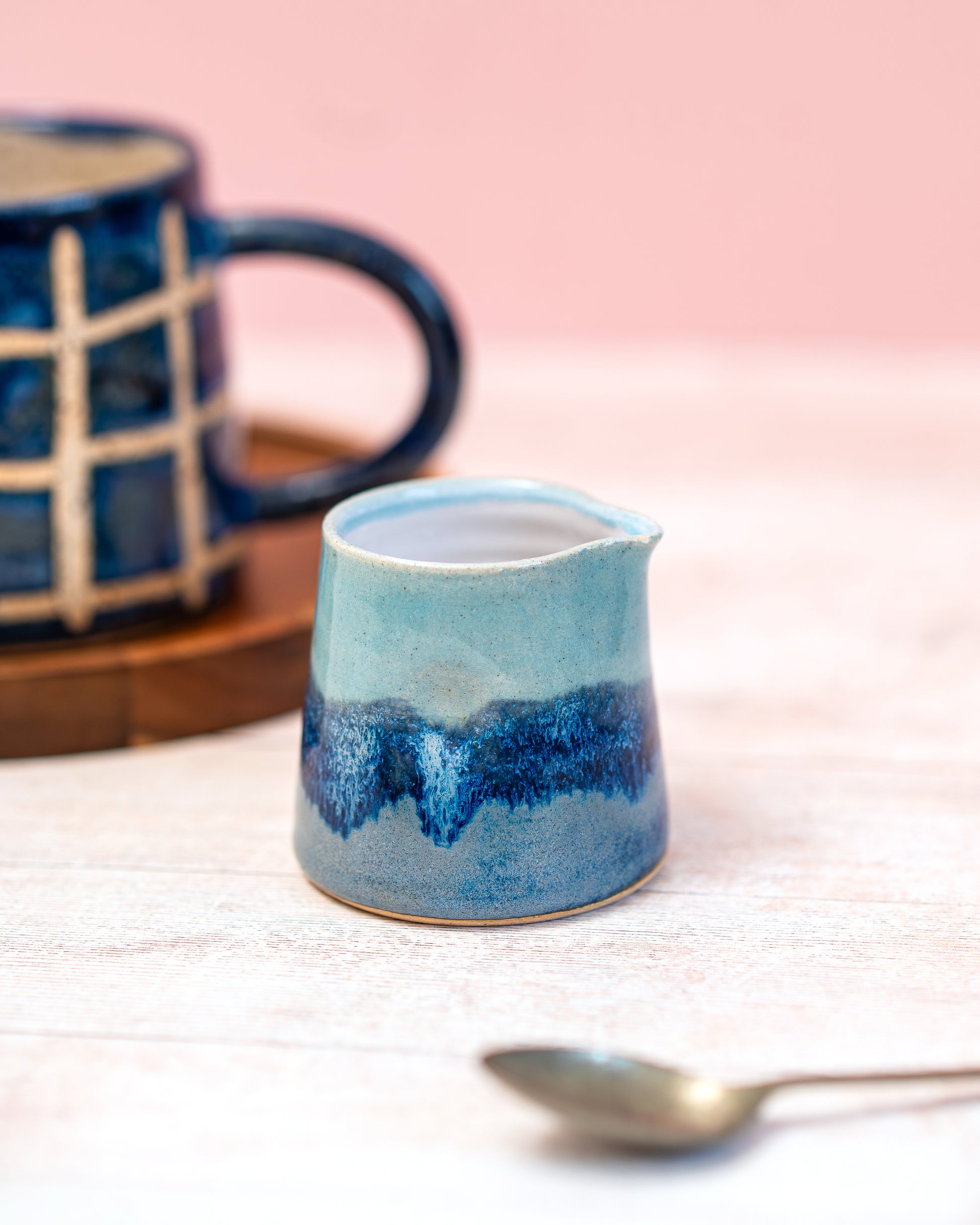 Blue ceramic pitcher on a white surface with a pink background