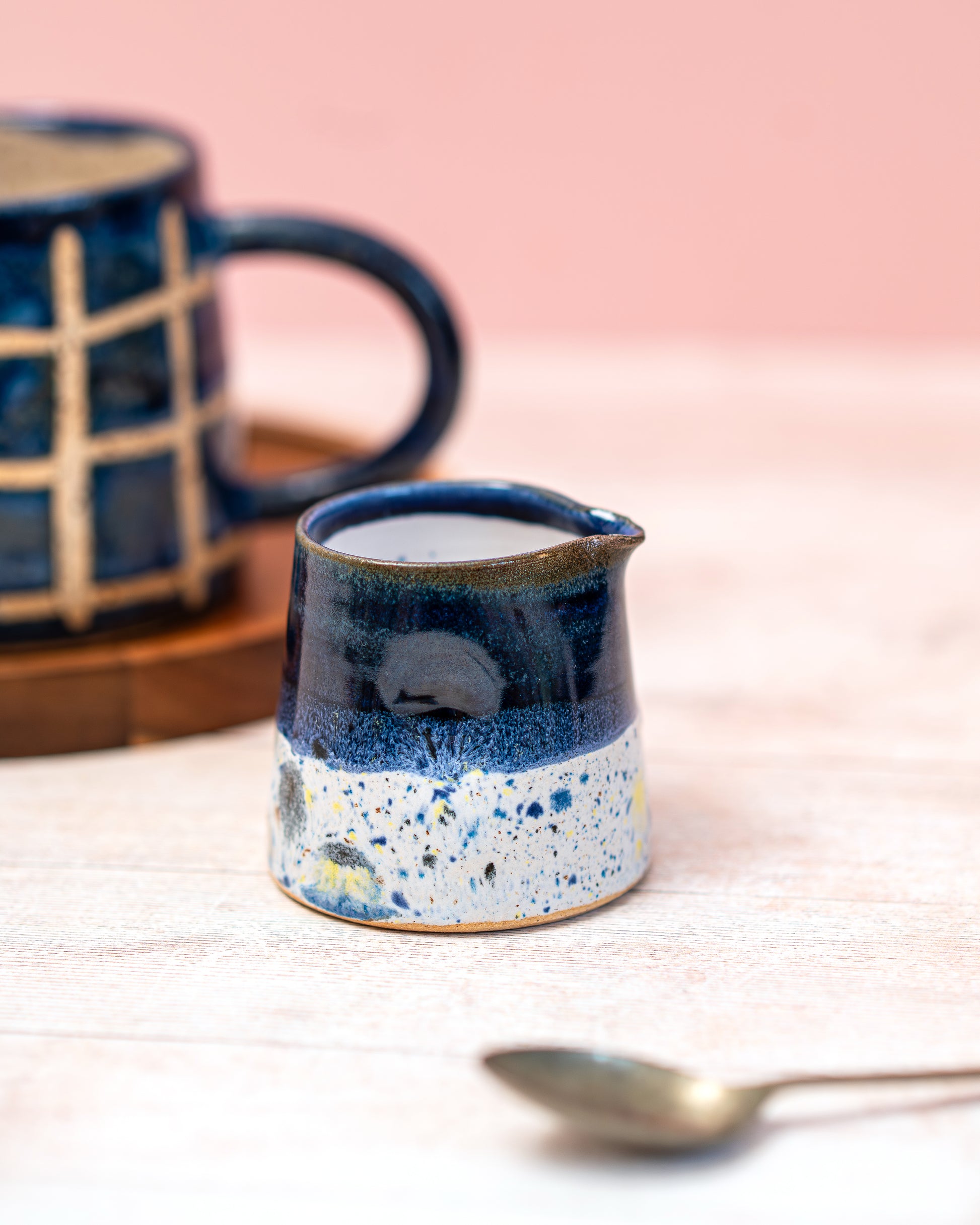 Blue ceramic mug with speckled design on a light surface with a pink background