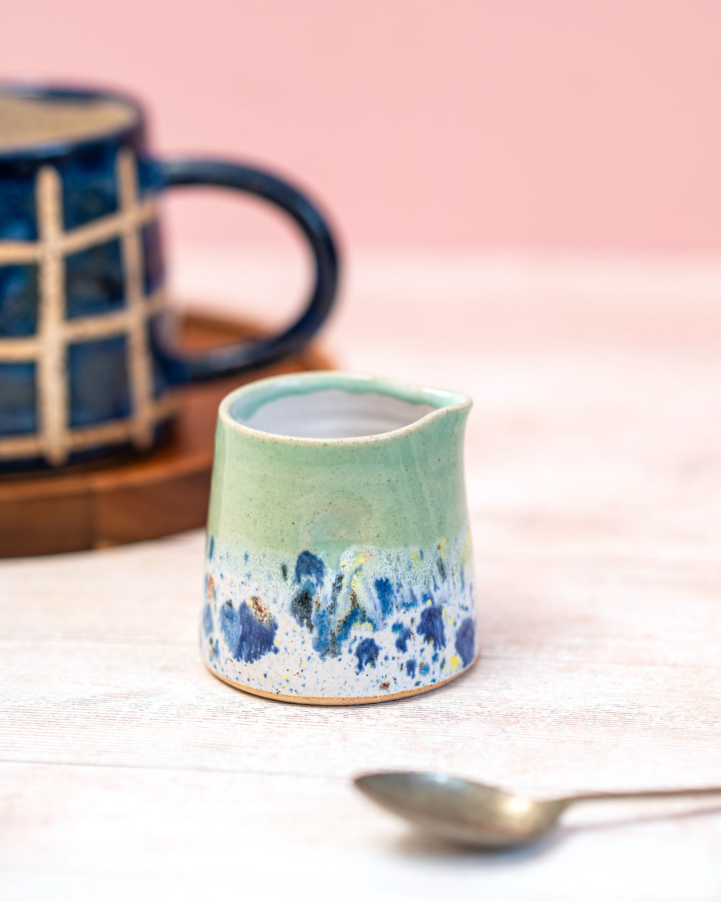 Green ceramic pitcher with blue speckles on a light pink background