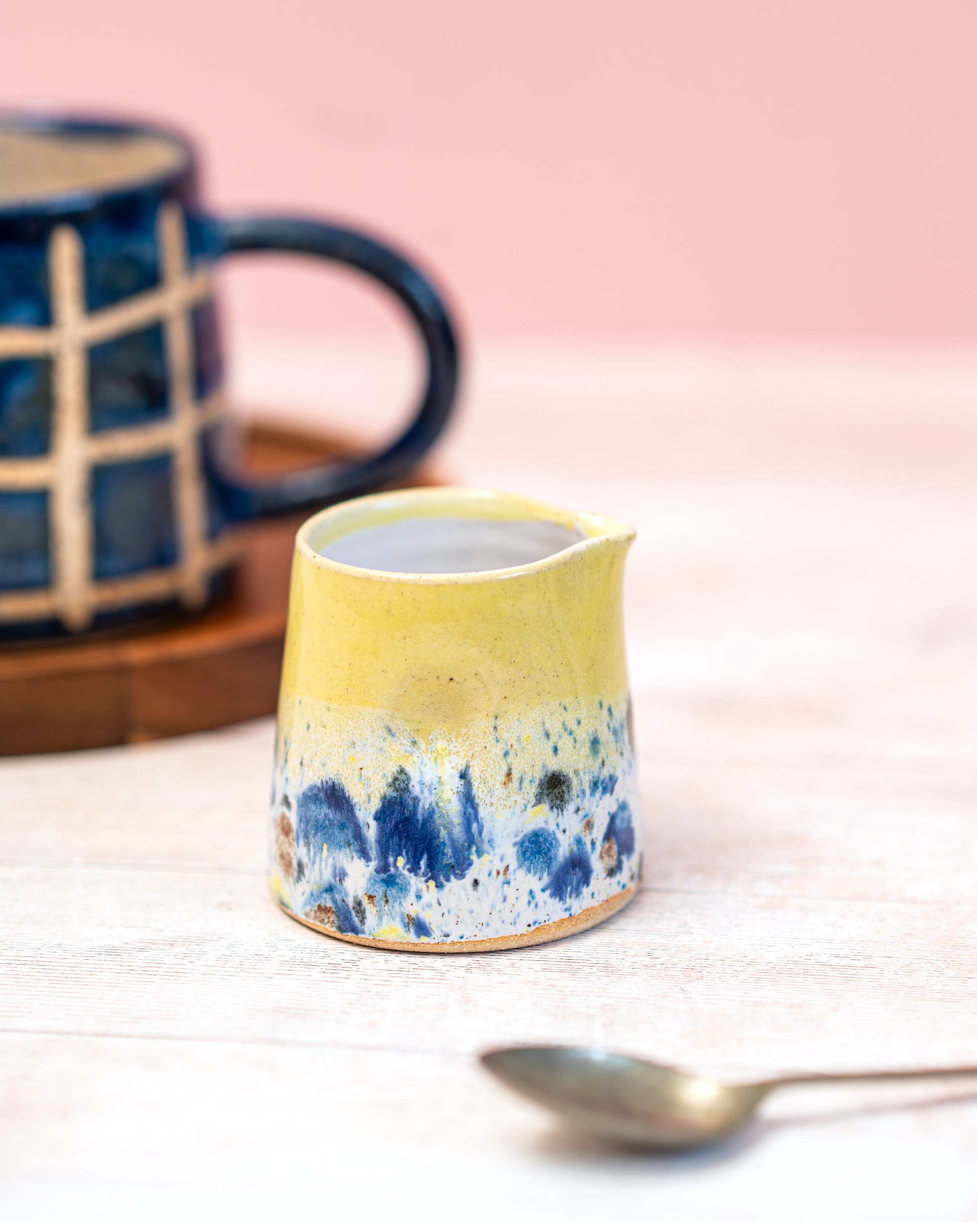 Yellow ceramic mug with blue abstract design on a light pink background
