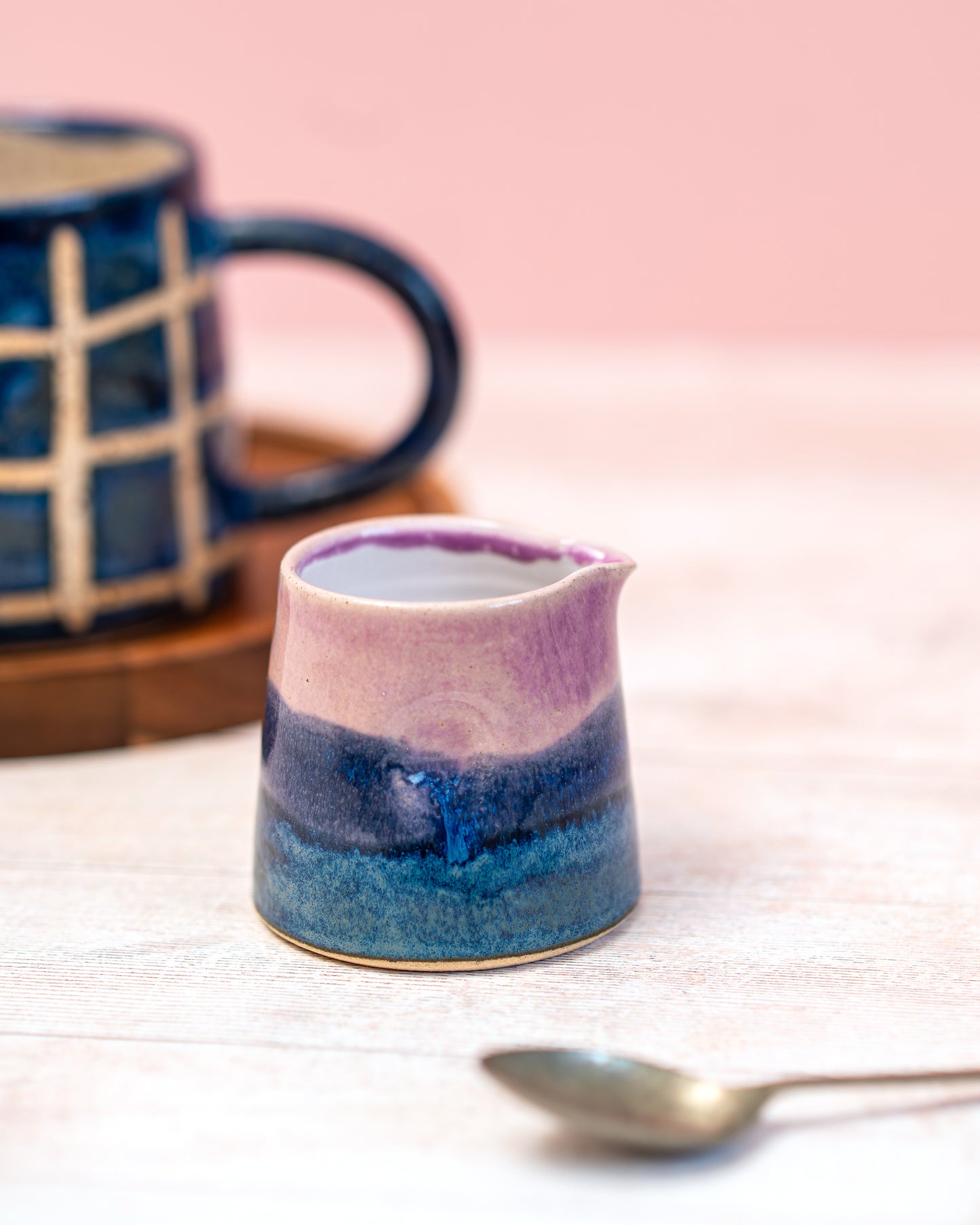 Small ceramic pitcher with two-tone design on a light surface with a pink background