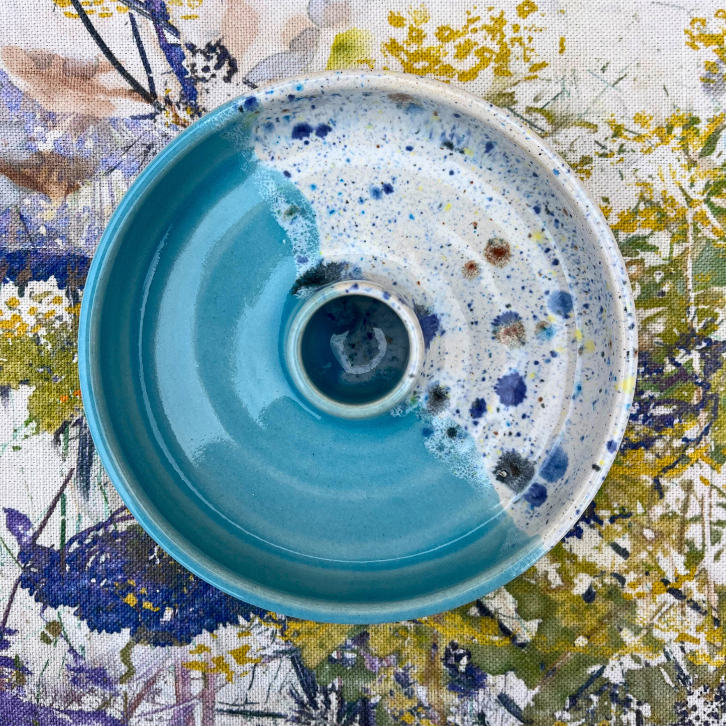 Blue ceramic candlestick holder with speckled pattern on a floral fabric background