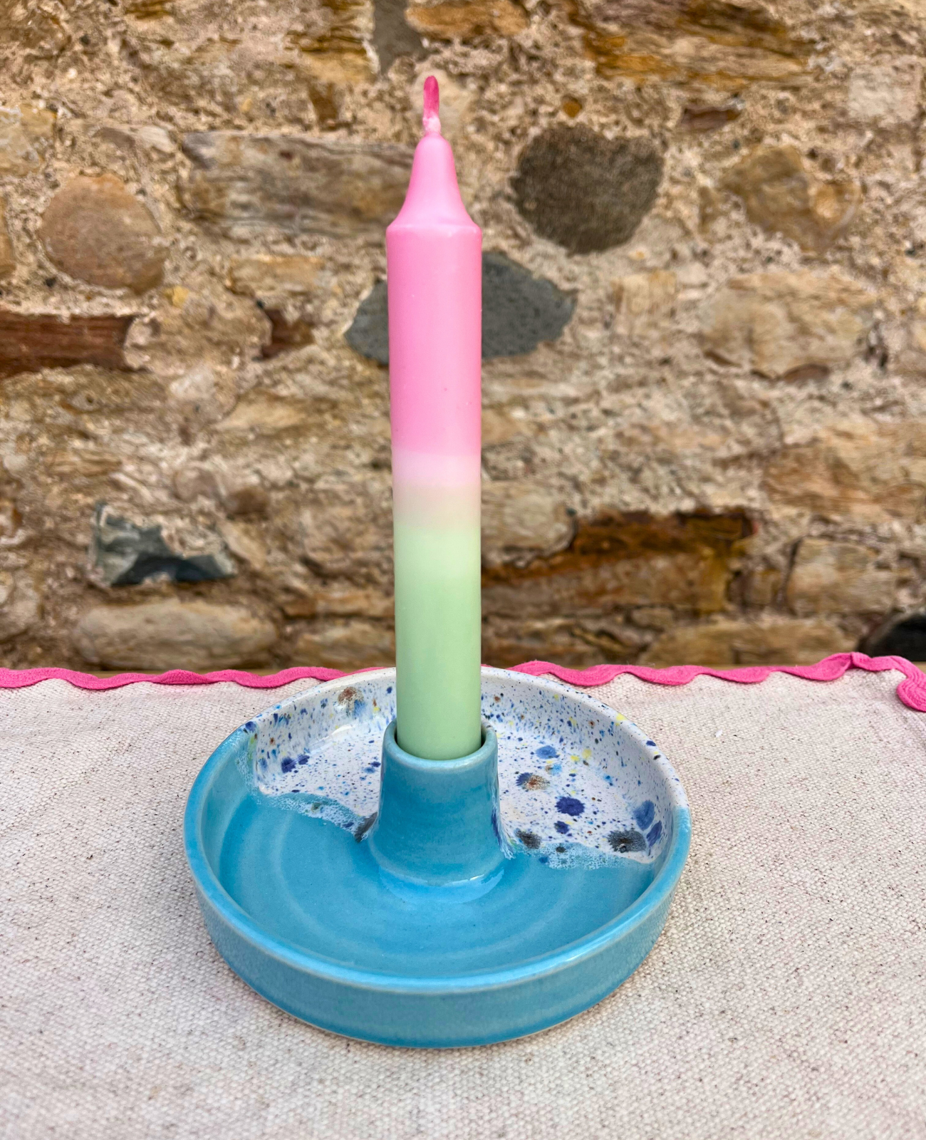 Colorful candle in a blue holder against a stone wall background