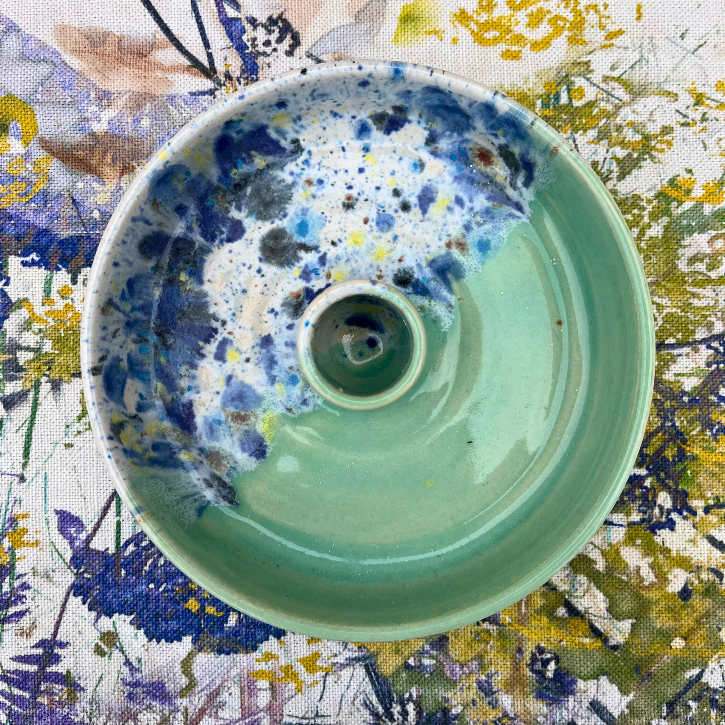 Ceramic candlestick holder with blue and green speckled design on a floral background