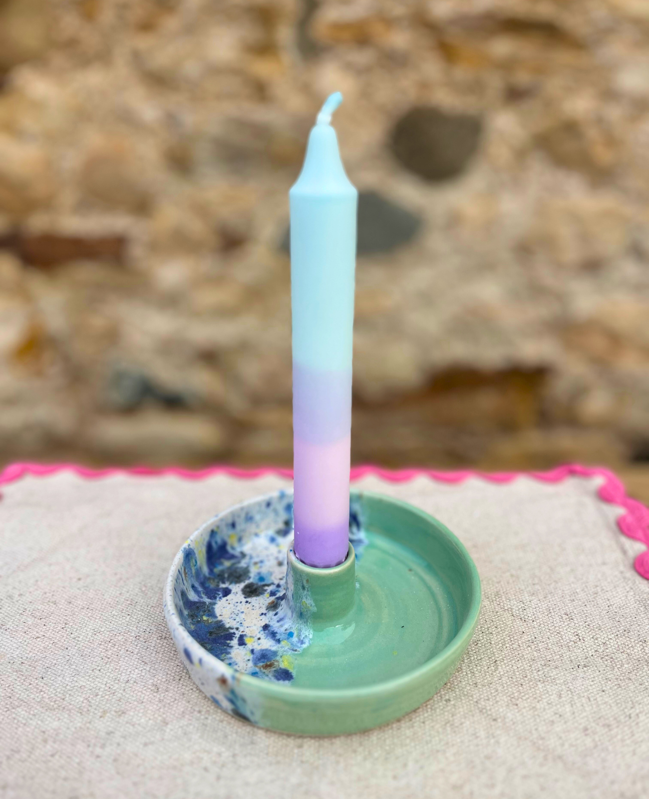Candle in a decorative holder on sand with a stone wall background