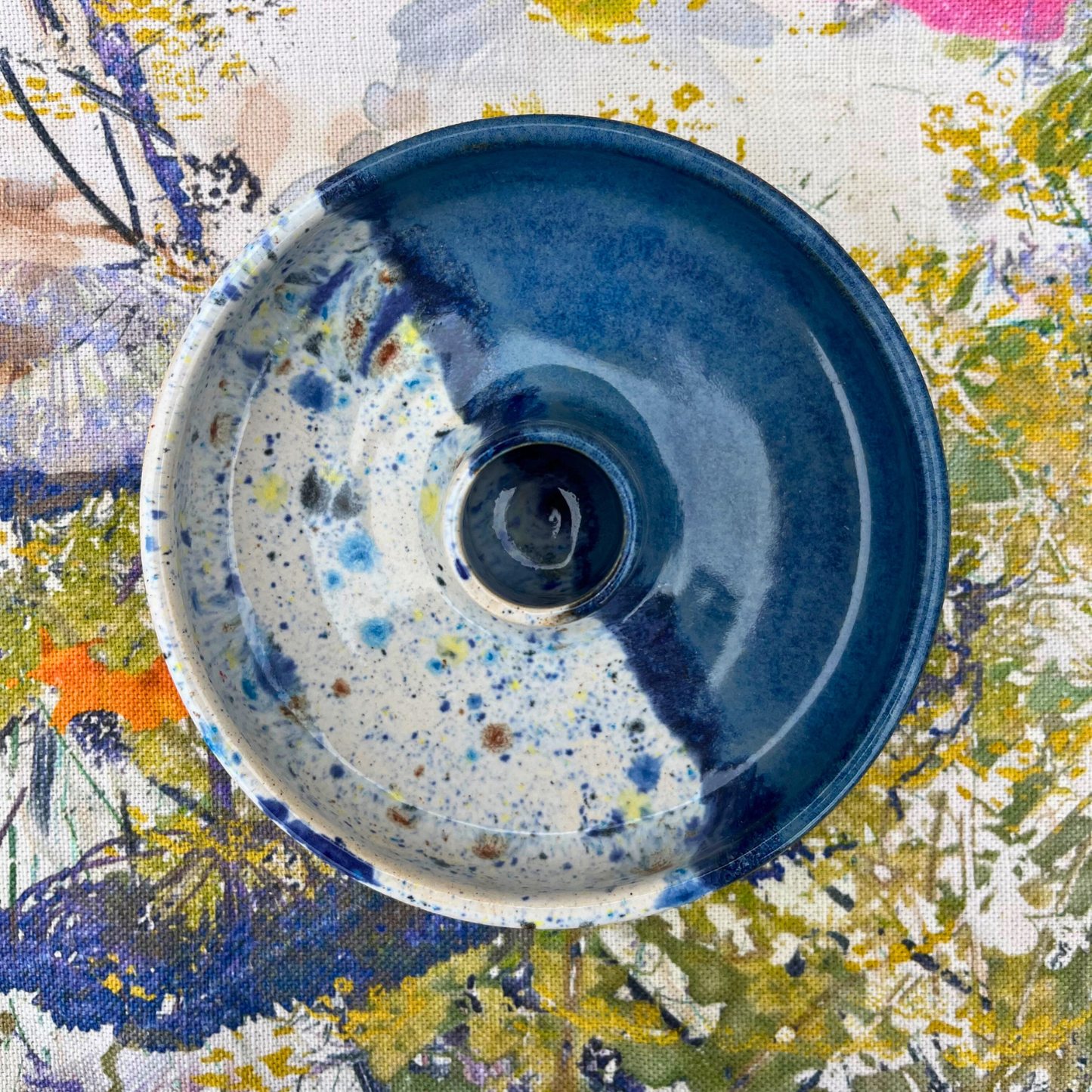 Ceramic candlestick holder with blue and white speckled design on a floral fabric background