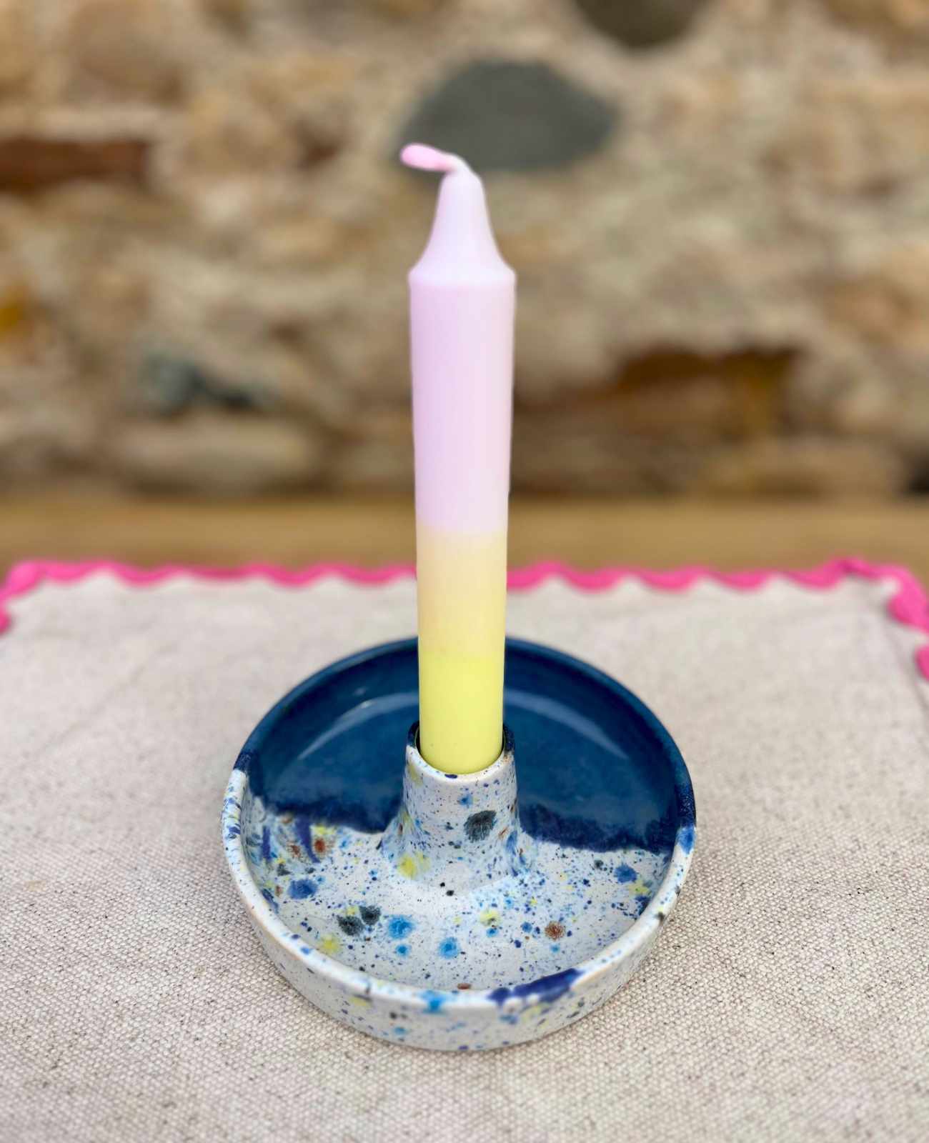 Candle in a blue and white speckled holder on a textured surface with a blurred natural background