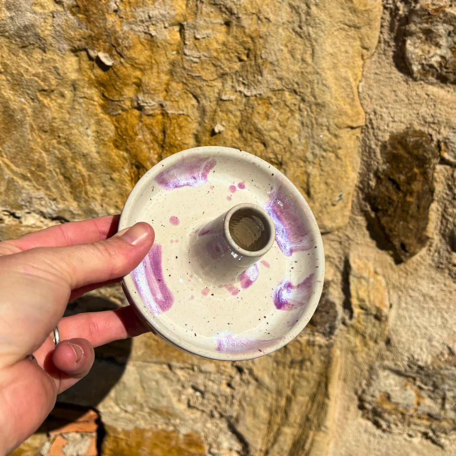 Ceramic candle holder with purple speckles held against a stone wall.