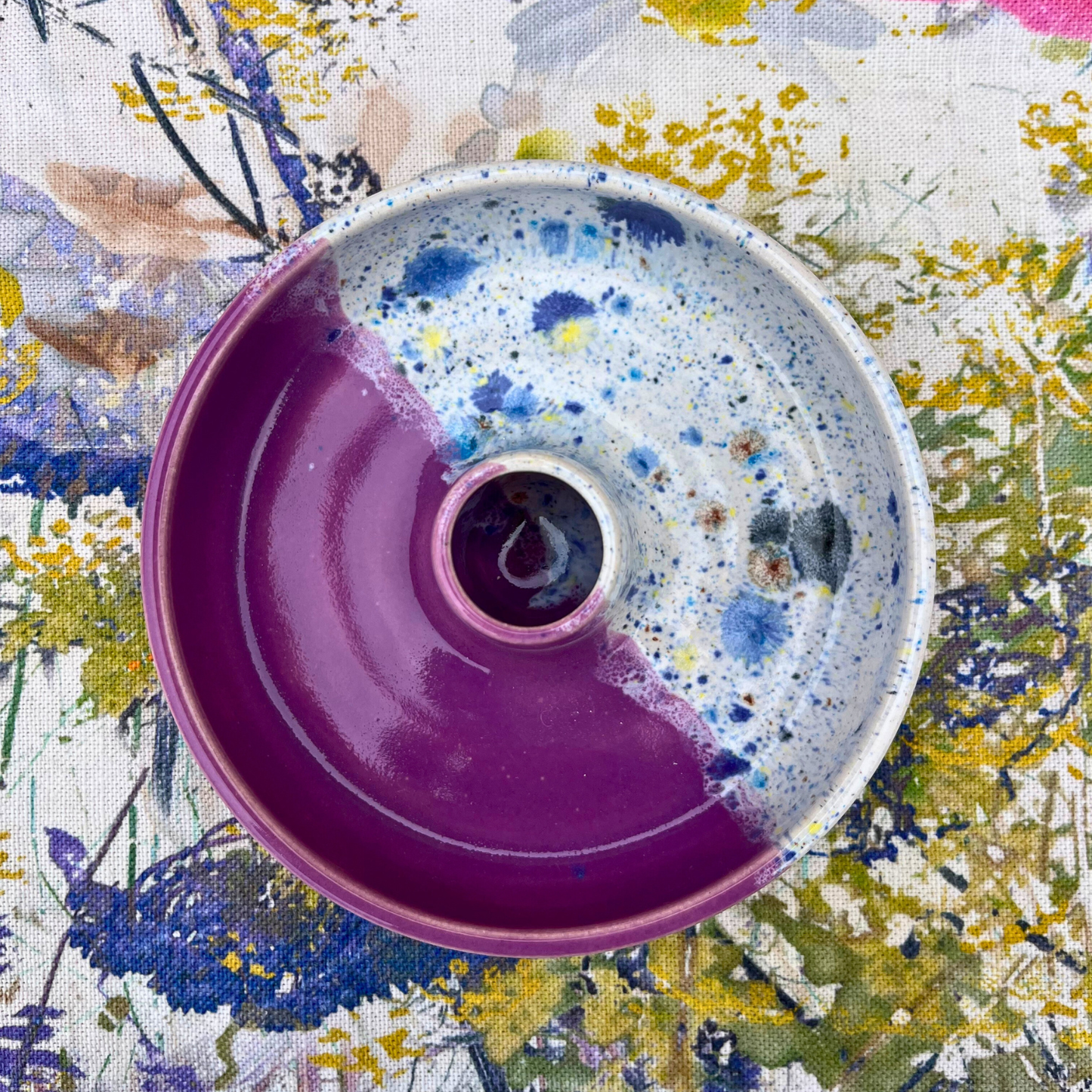 Ceramic candlestick holder with pink base and white speckled top on a floral background