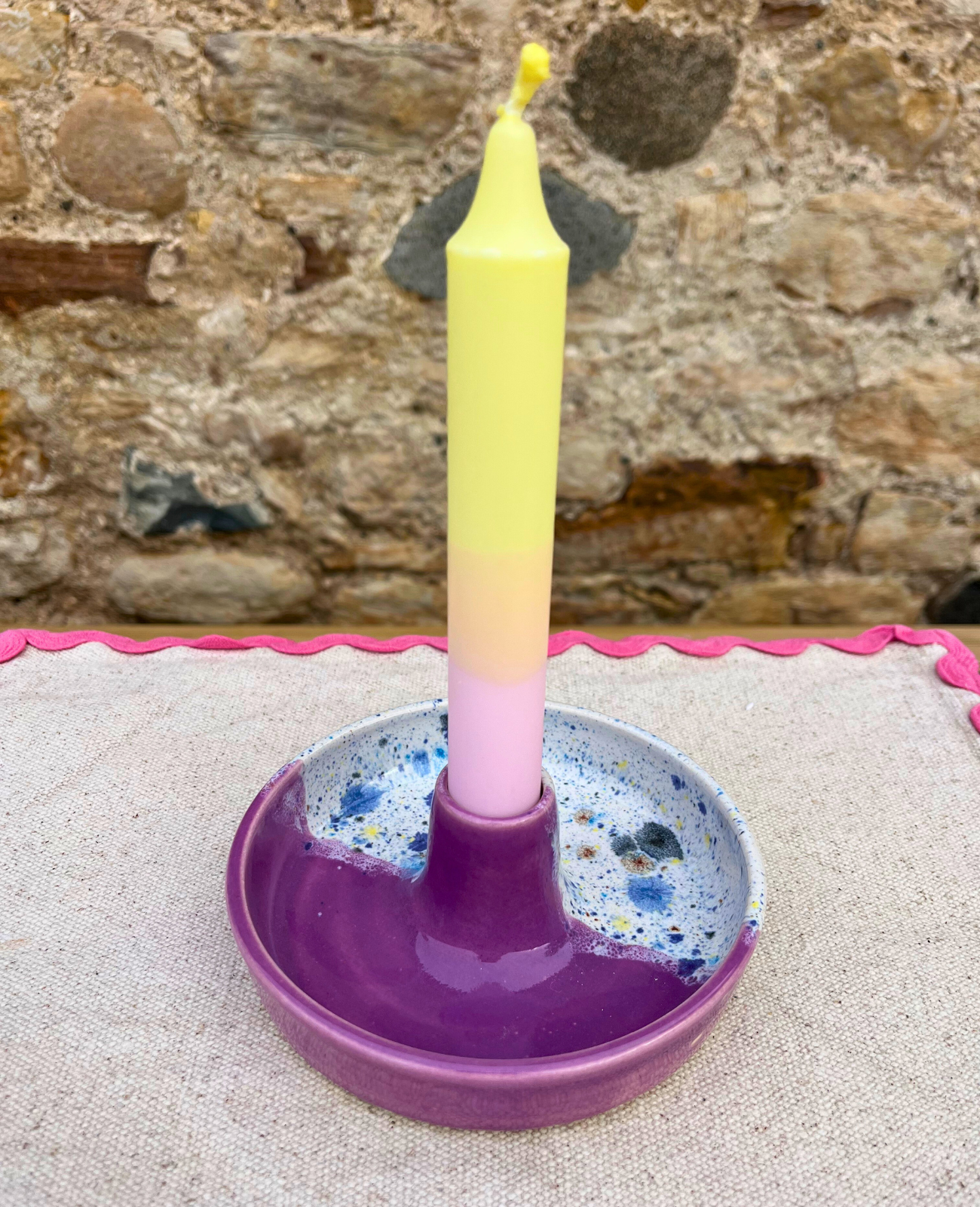 Colorful candle in a purple holder on a textured surface with a stone wall background