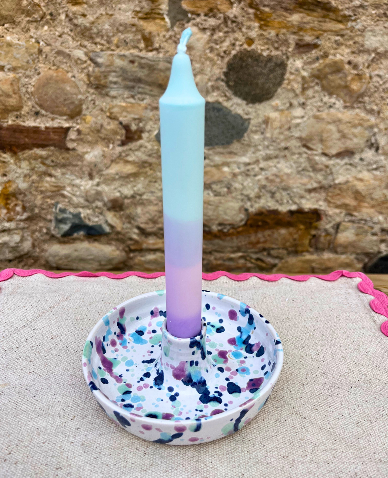 Gradient candle in a terrazzo-patterned holder against a stone wall background