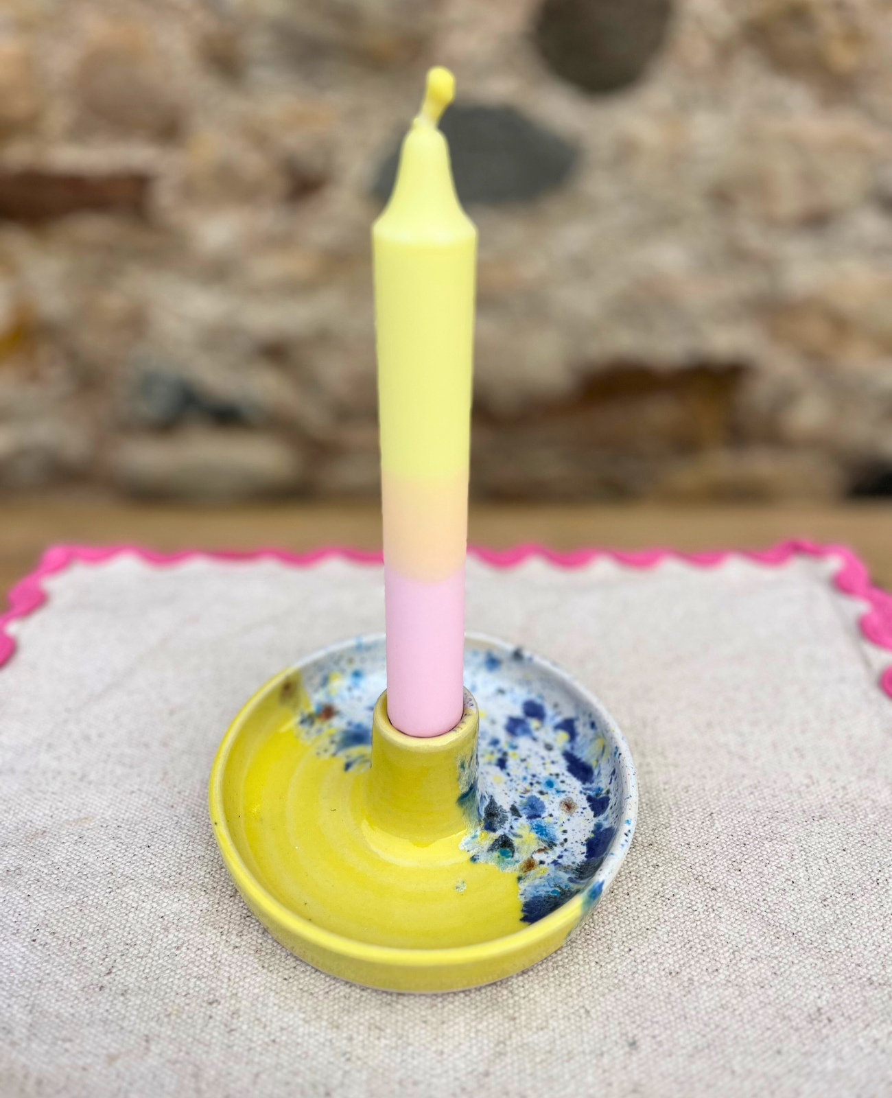 Yellow candle in a decorative holder on a textured surface with a blurred natural background