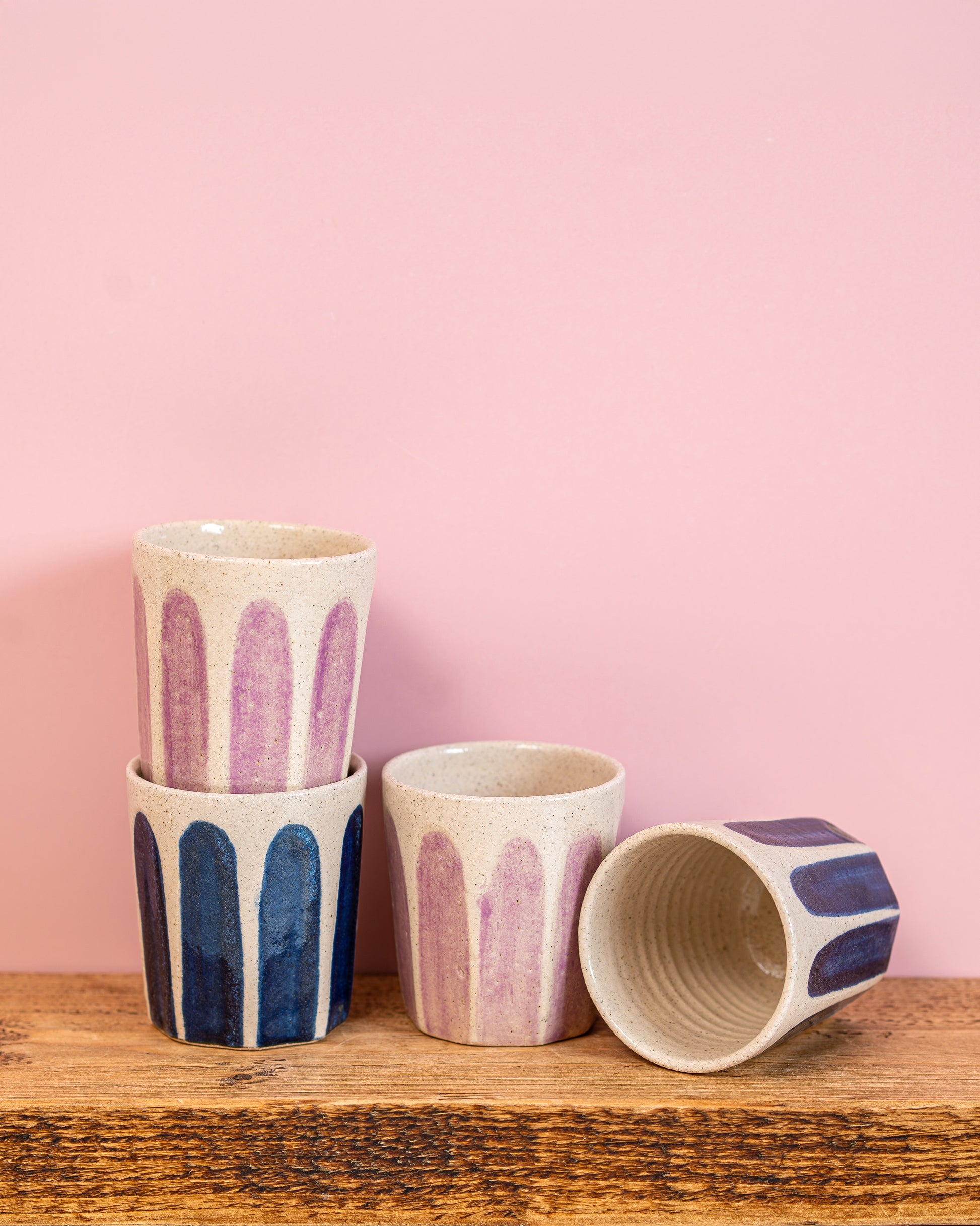 Set of ceramic cups with abstract patterns on a wooden surface and pink background