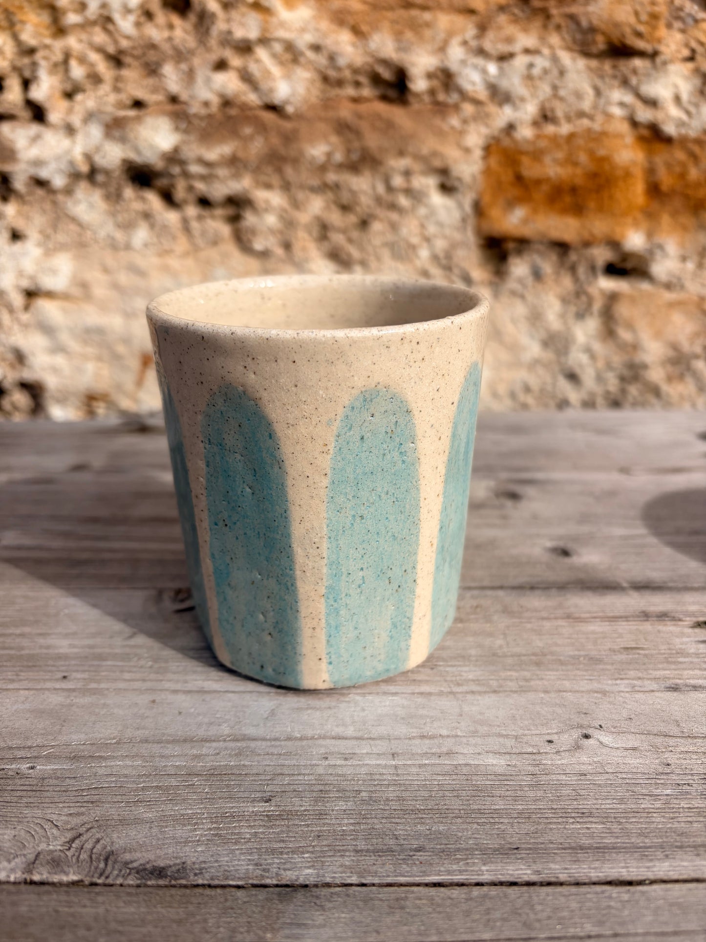 Ceramic cup with blue accents on a wooden surface with a stone wall background