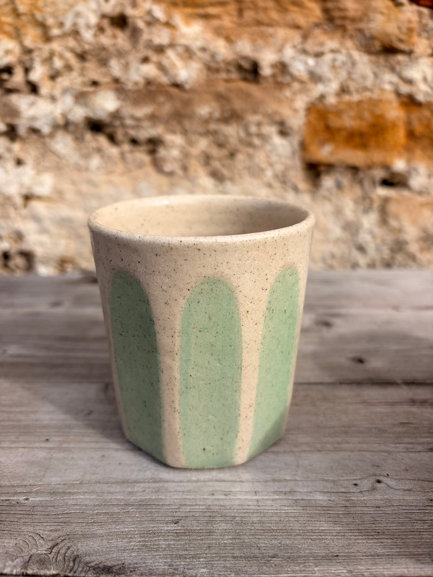Ceramic cup with green and beige design on a wooden surface with stone wall background