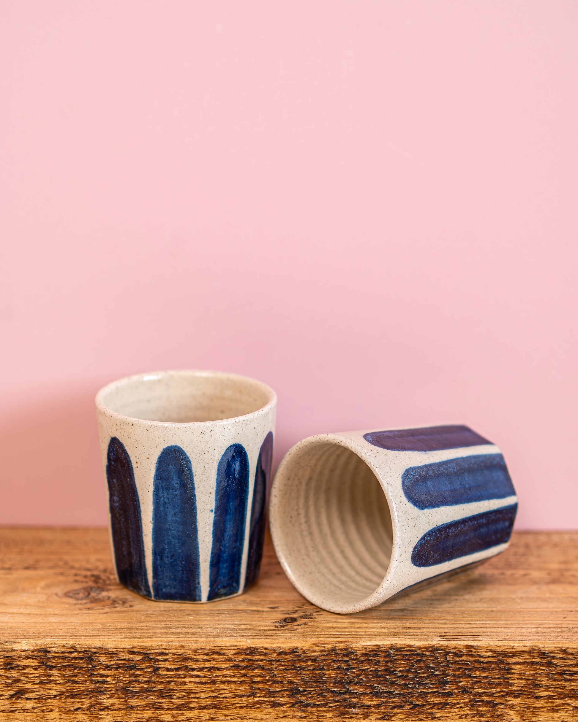 Two ceramic cups with blue patterns on a wooden surface against a pink background