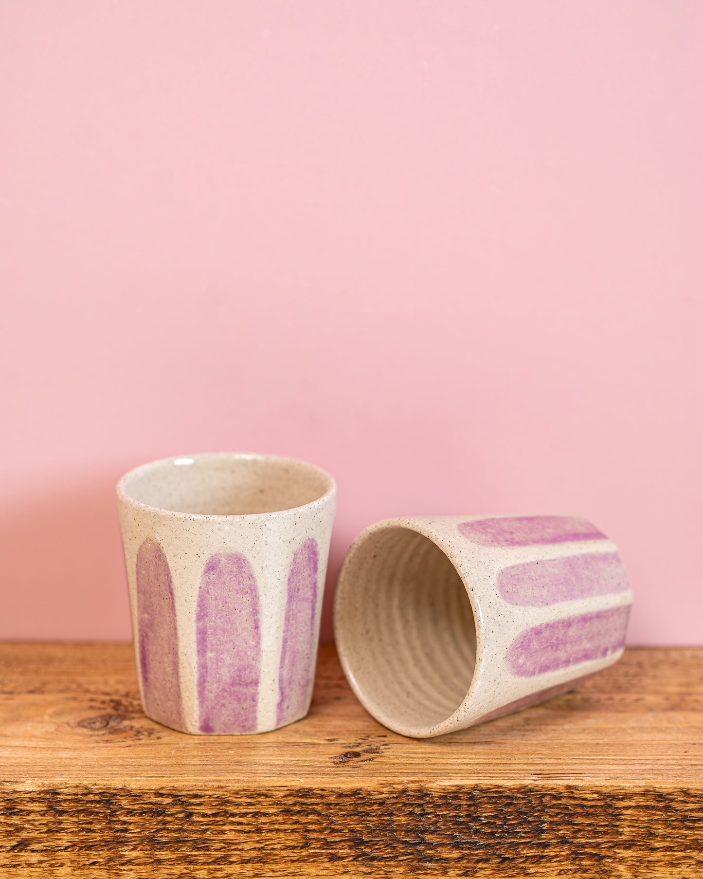 Two ceramic cups with purple abstract patterns on a wooden surface and pink background