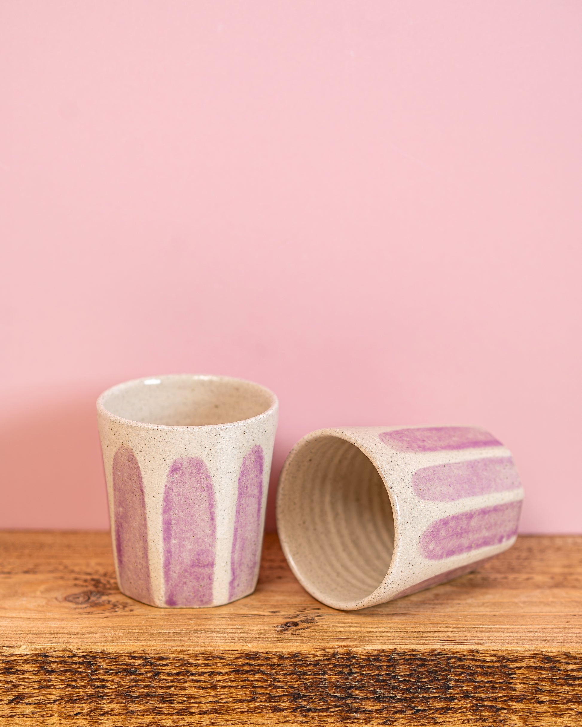 Two ceramic cups with purple abstract patterns on a wooden surface and pink background