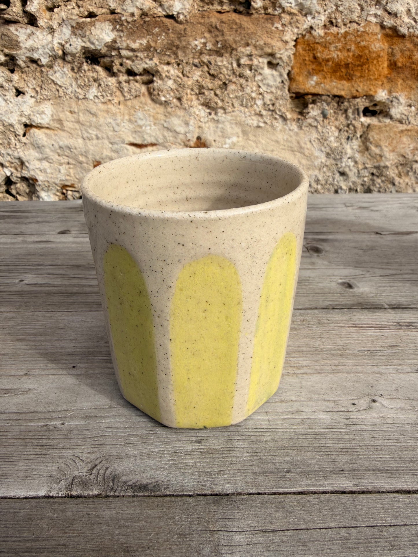 Ceramic cylindrical object with yellow accent against a stone wall and wooden surface