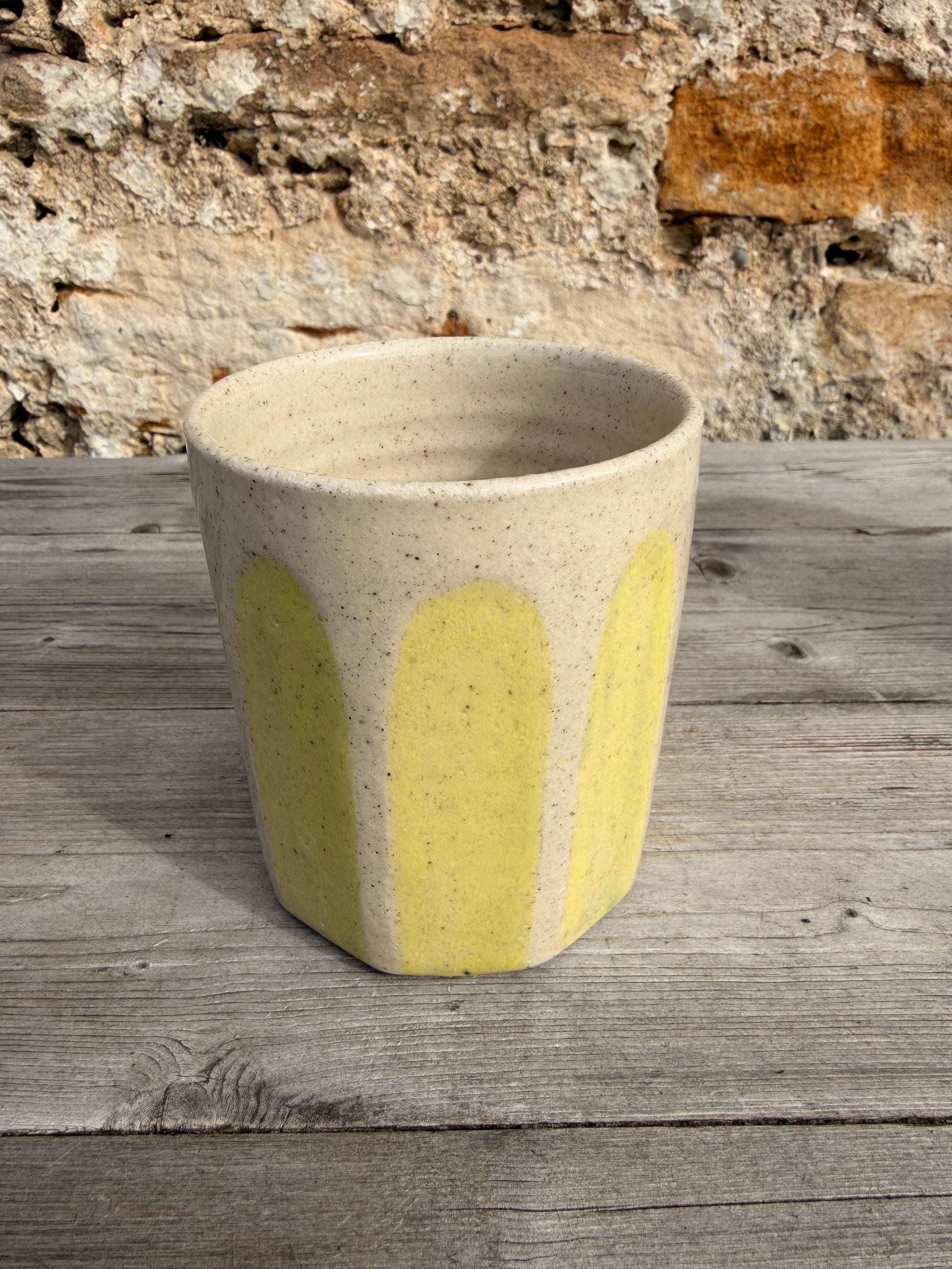 Ceramic cylindrical object with yellow accent against a stone wall and wooden surface