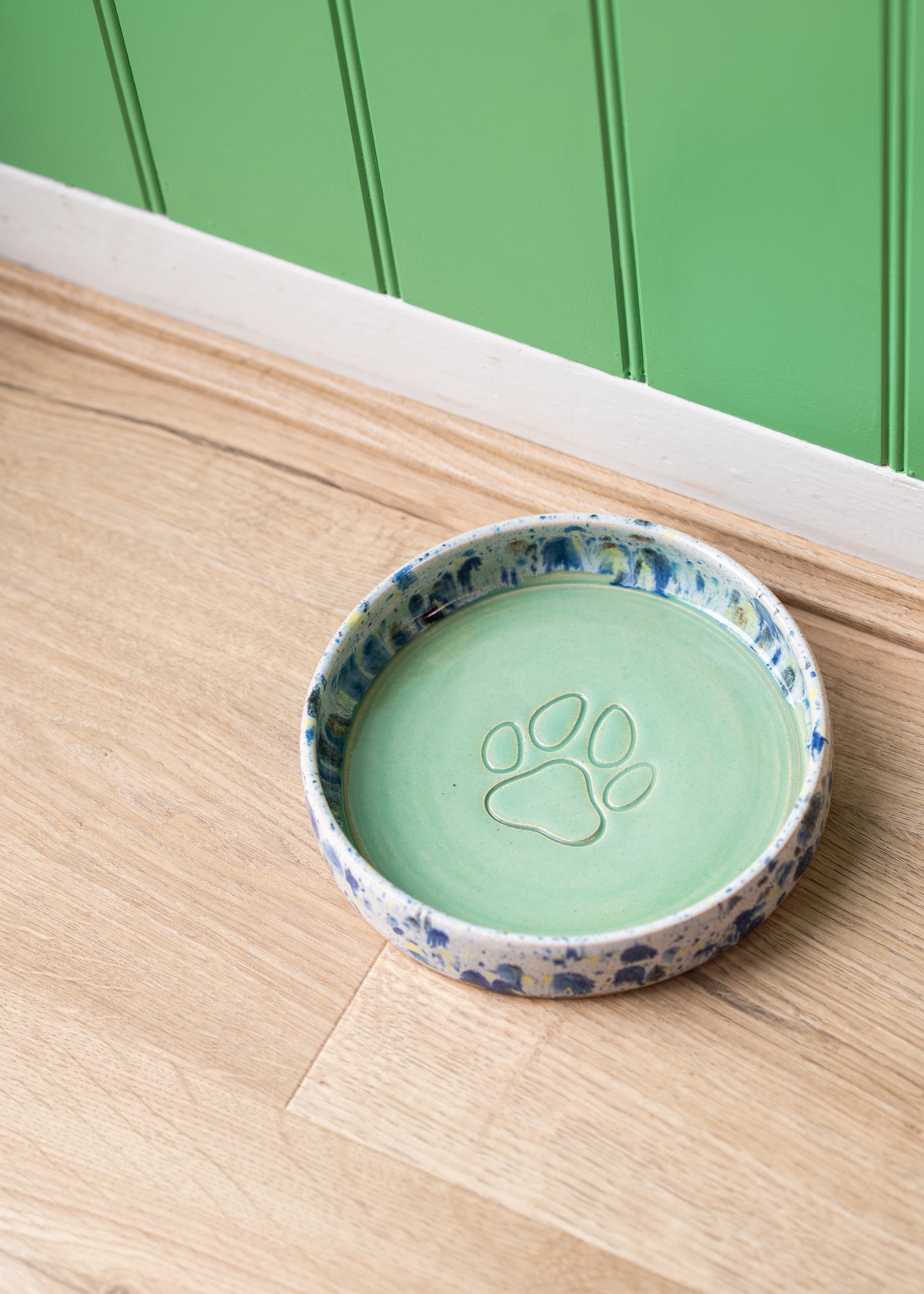 Green dog bowl with a paw print design on a wooden surface.
