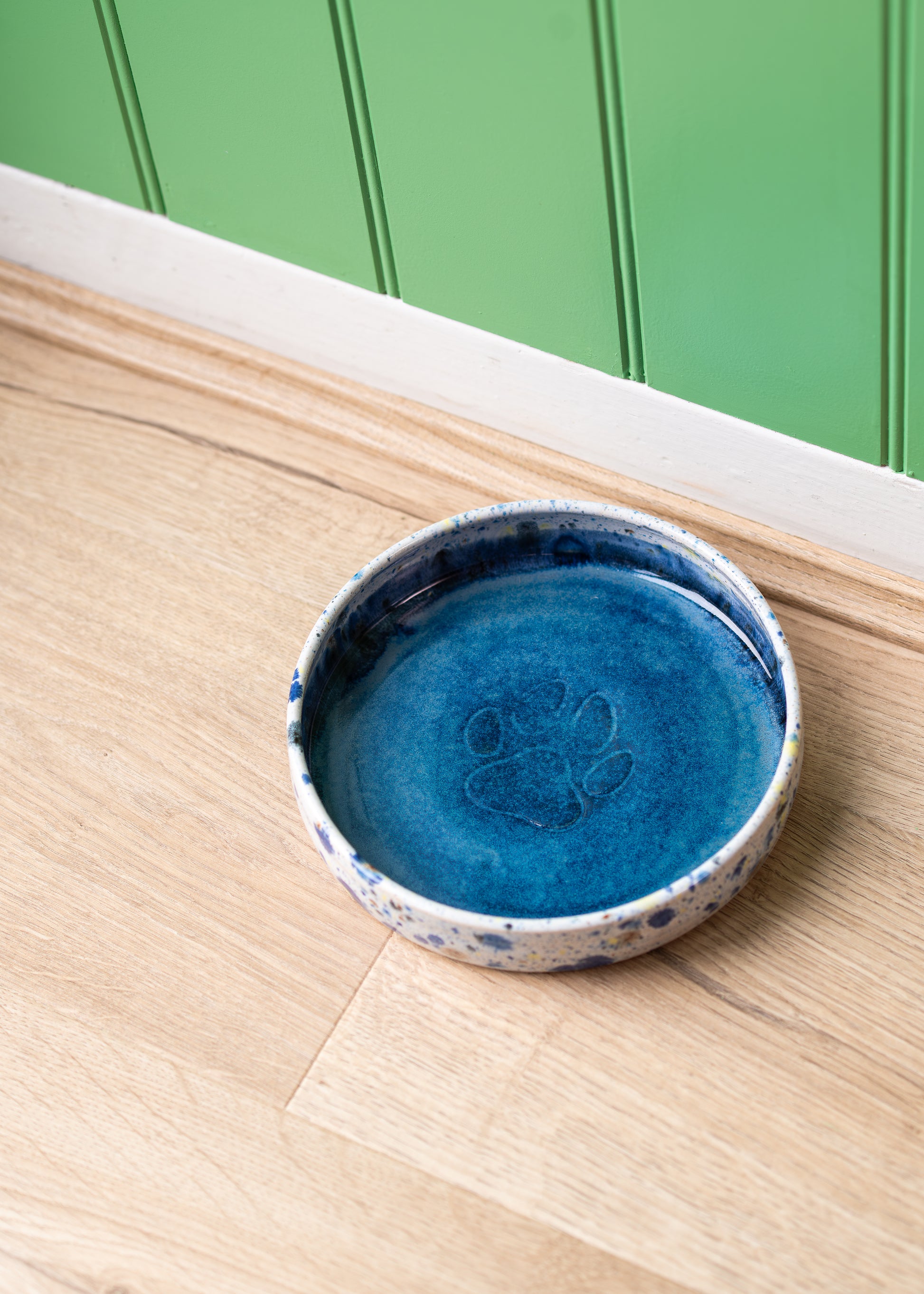 Blue ceramic dish with paw print design on a wooden surface against a green wall.