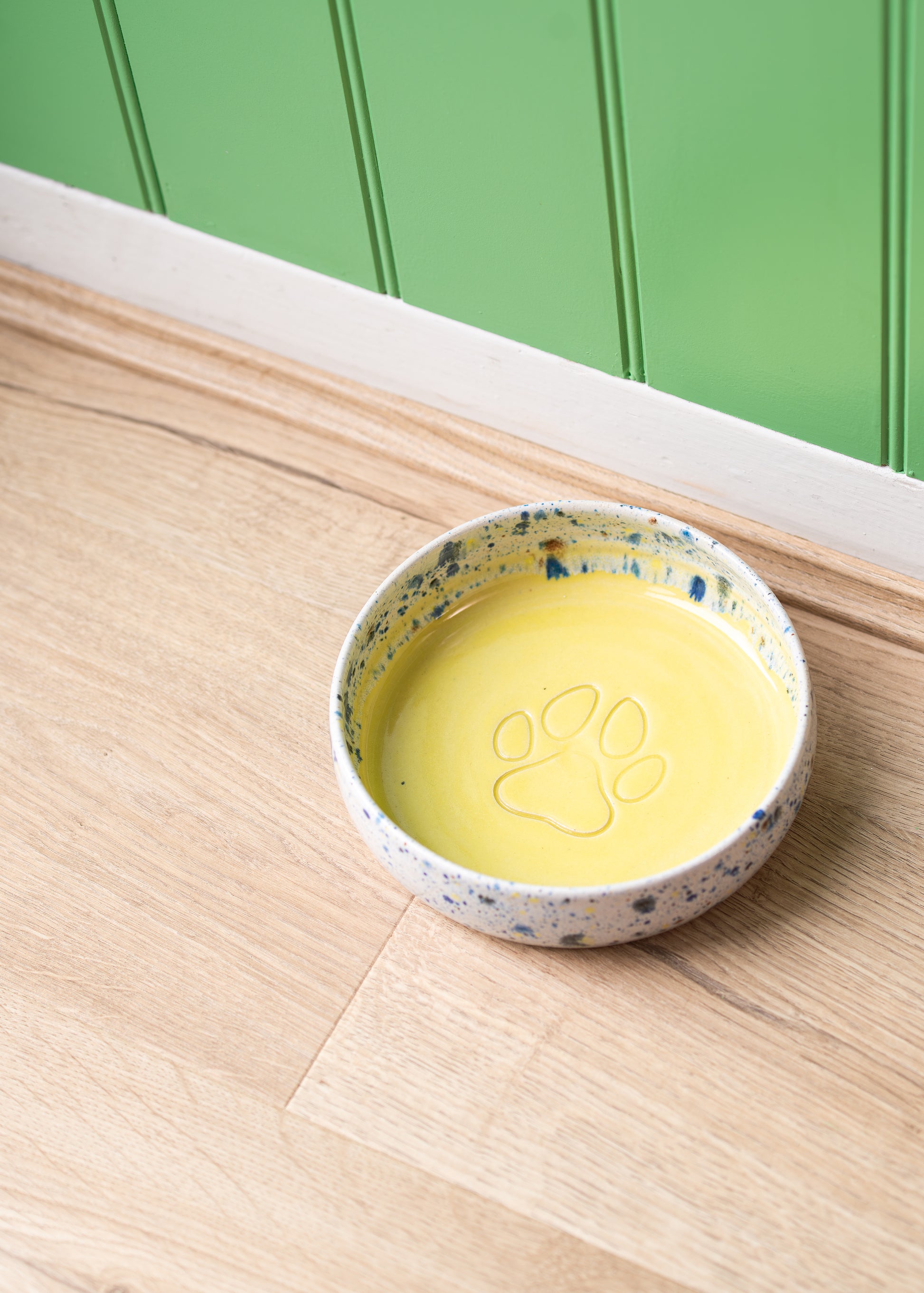 Yellow dog bowl on a wooden surface and green wall background